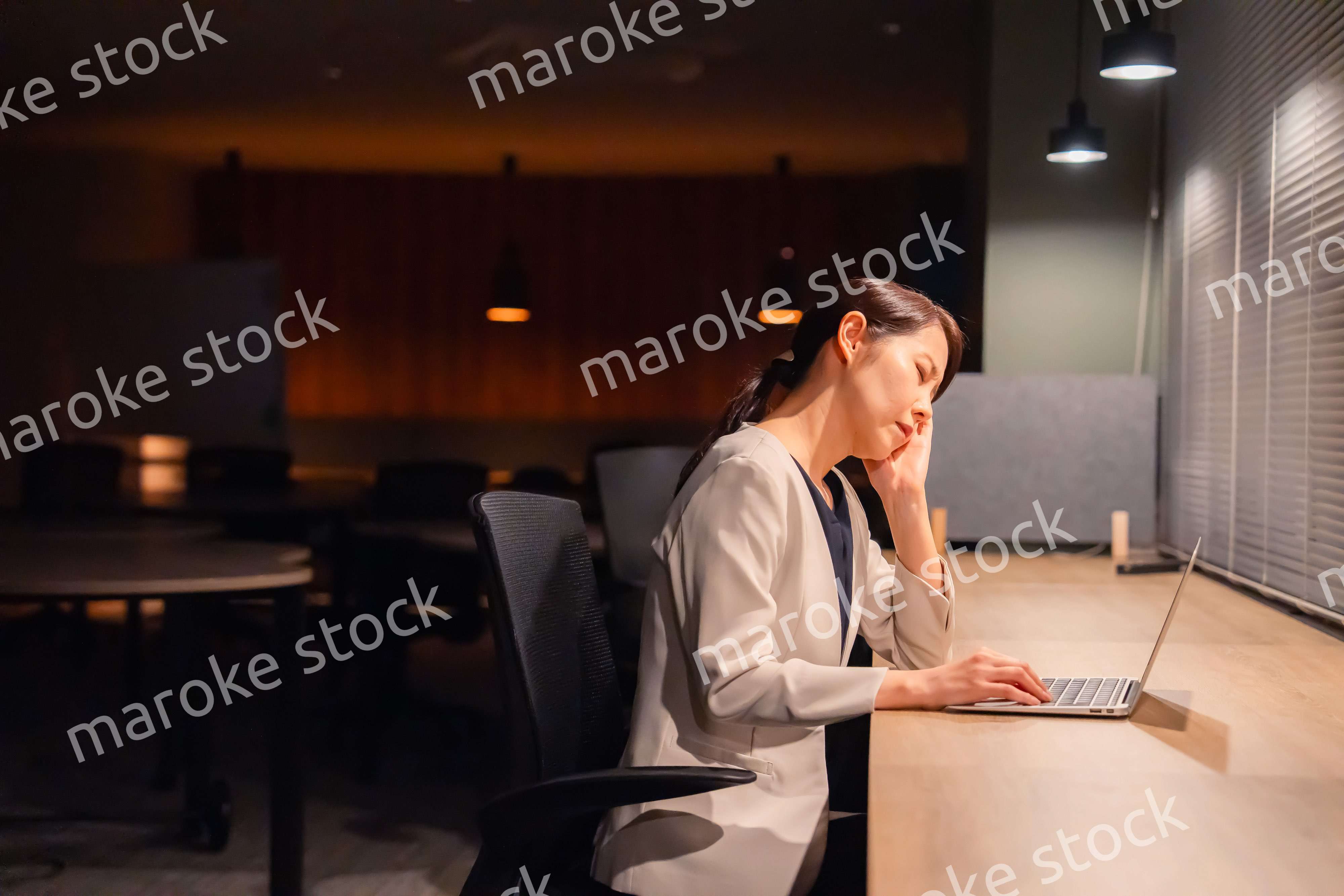 オフィスで暗くなるまで残業をして疲れる女性管理職