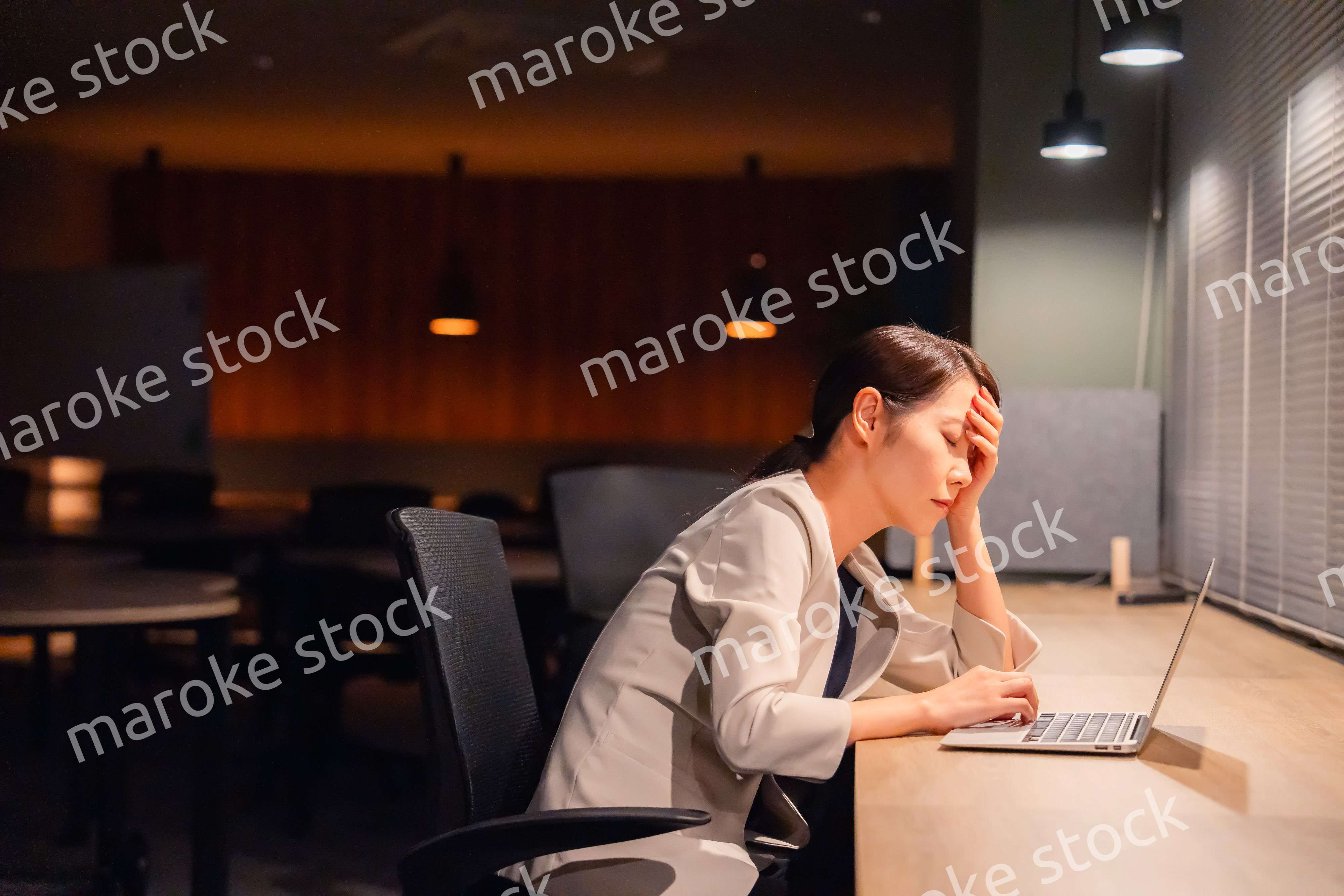 オフィスで暗くなるまで残業をして疲れる女性管理職