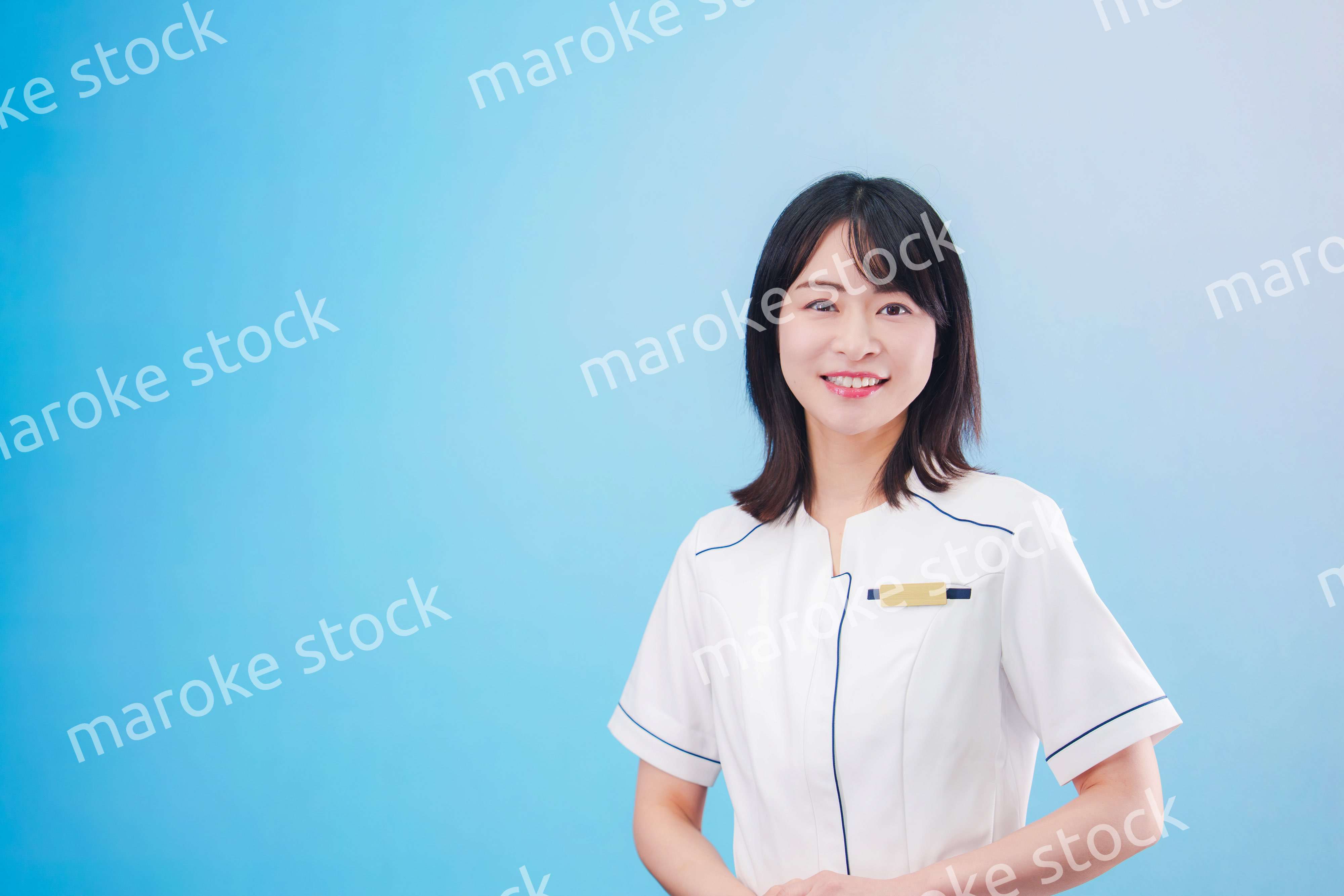 クリニックの受付をする若い女性スタッフ（水色背景）