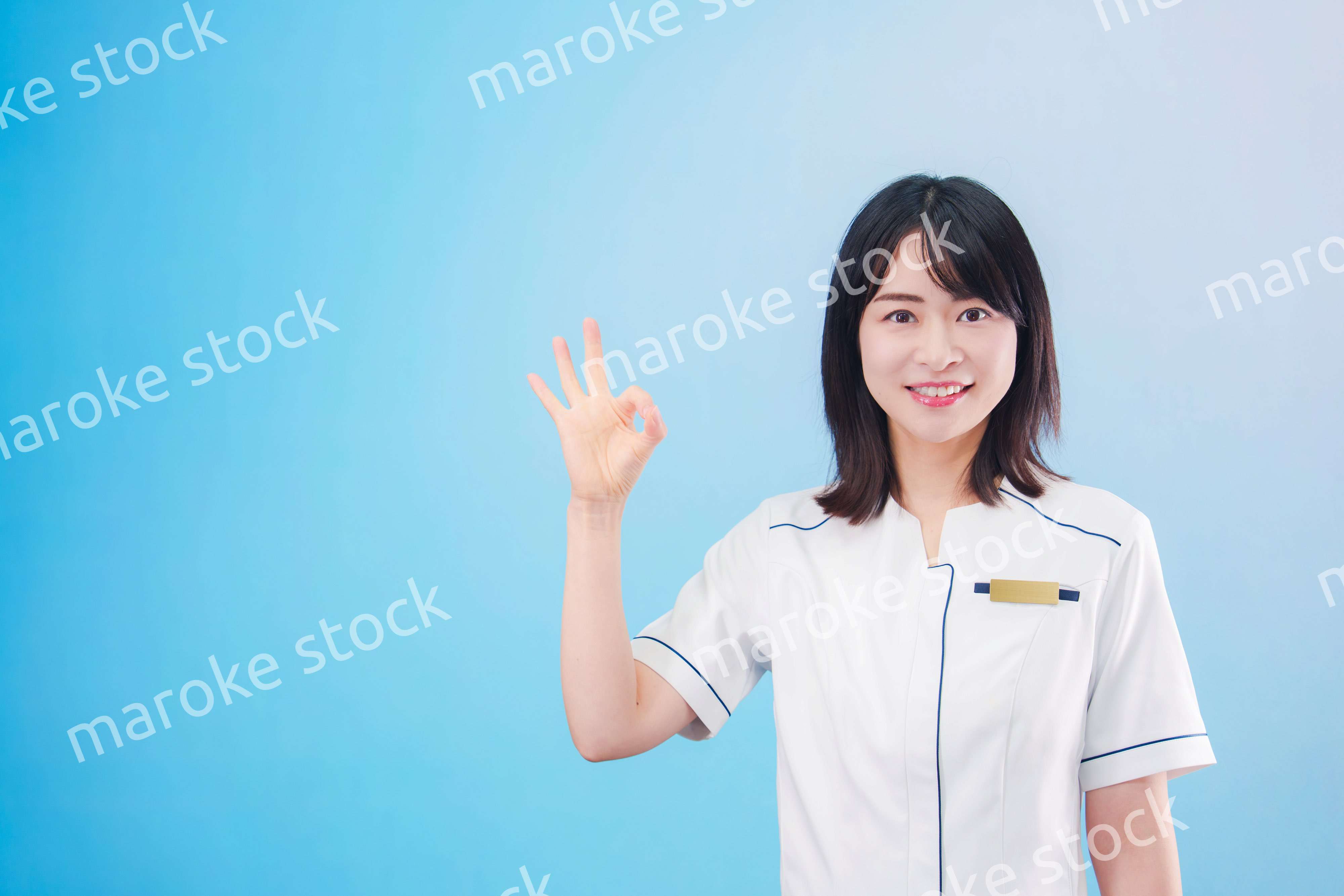 クリニックの受付をする若い女性スタッフ（水色背景）