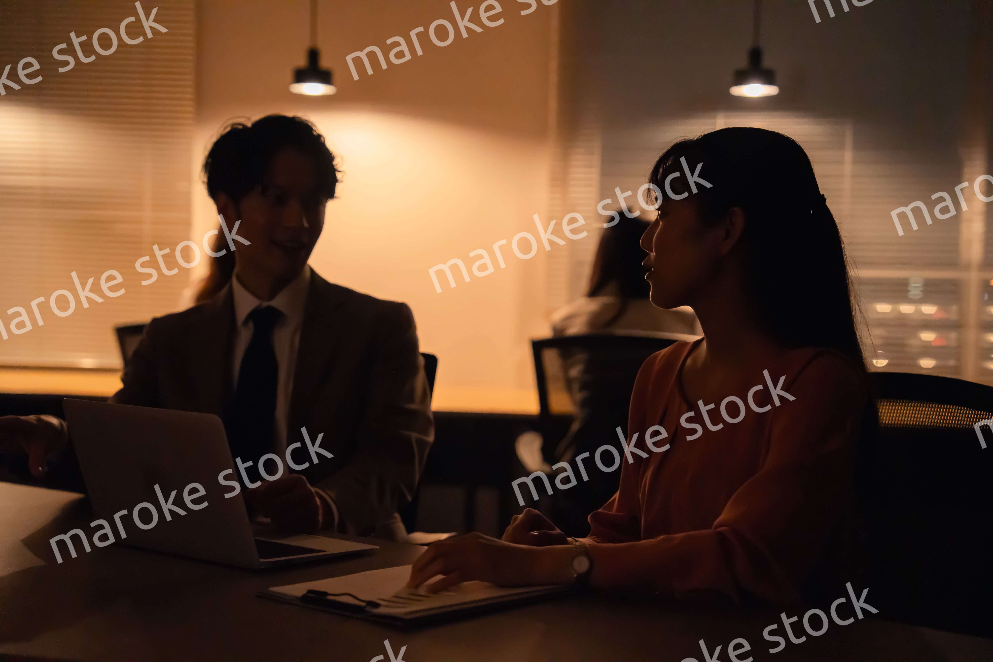 多忙で照明が消えたあとも仕事をする男女のビジネスパーソン