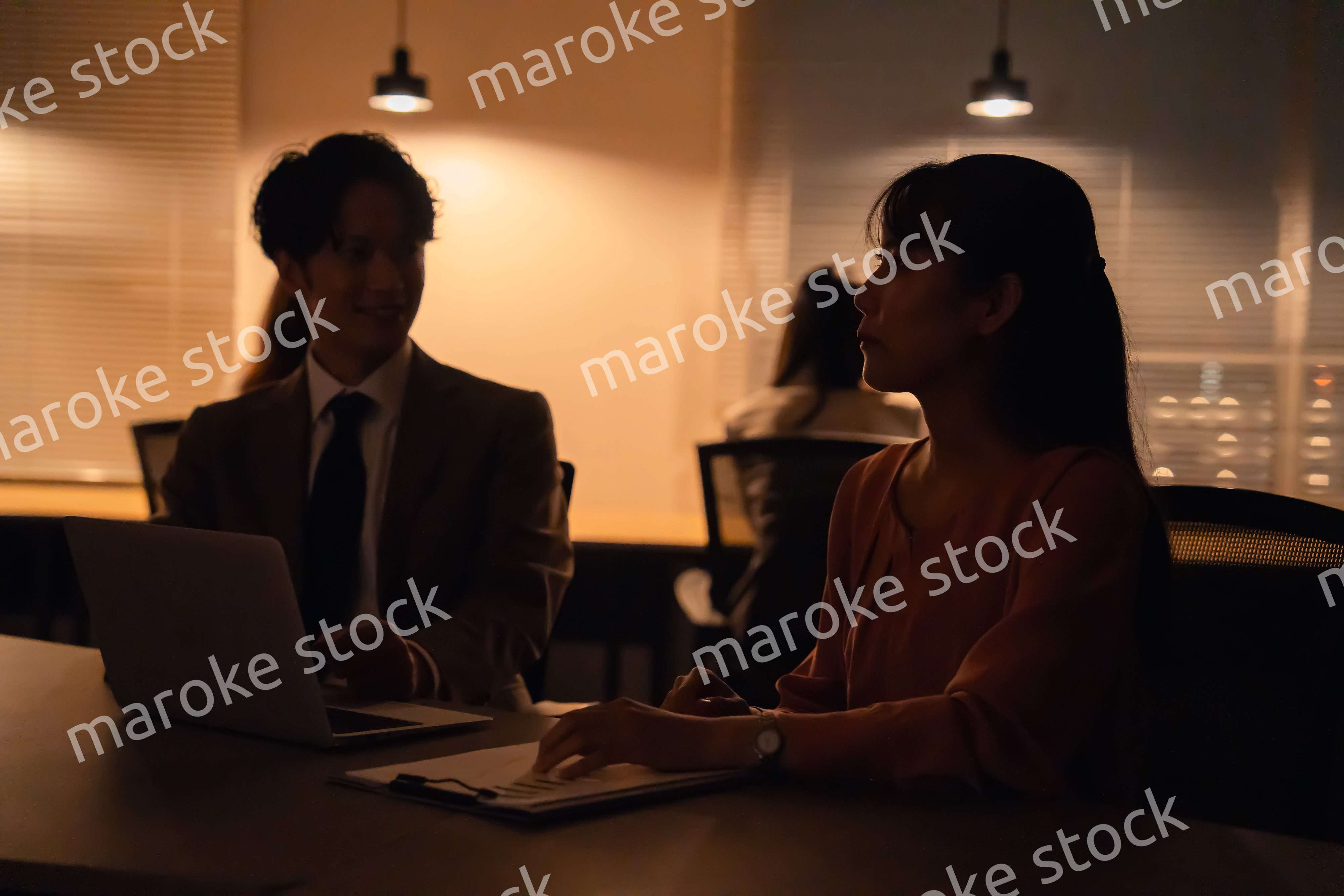 多忙で照明が消えたあとも仕事をする男女のビジネスパーソン