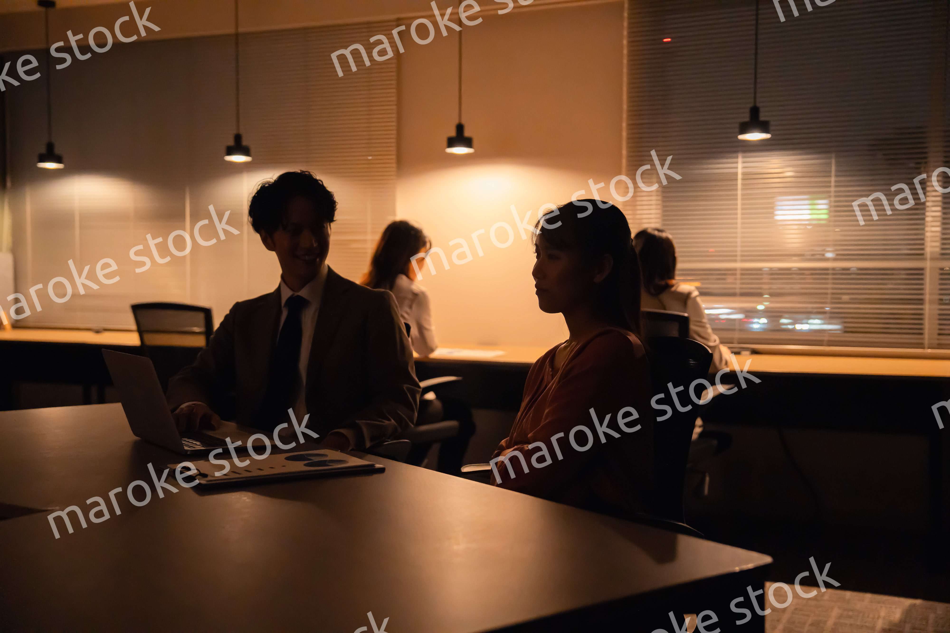 多忙で照明が消えたあとも仕事をする男女のビジネスパーソン