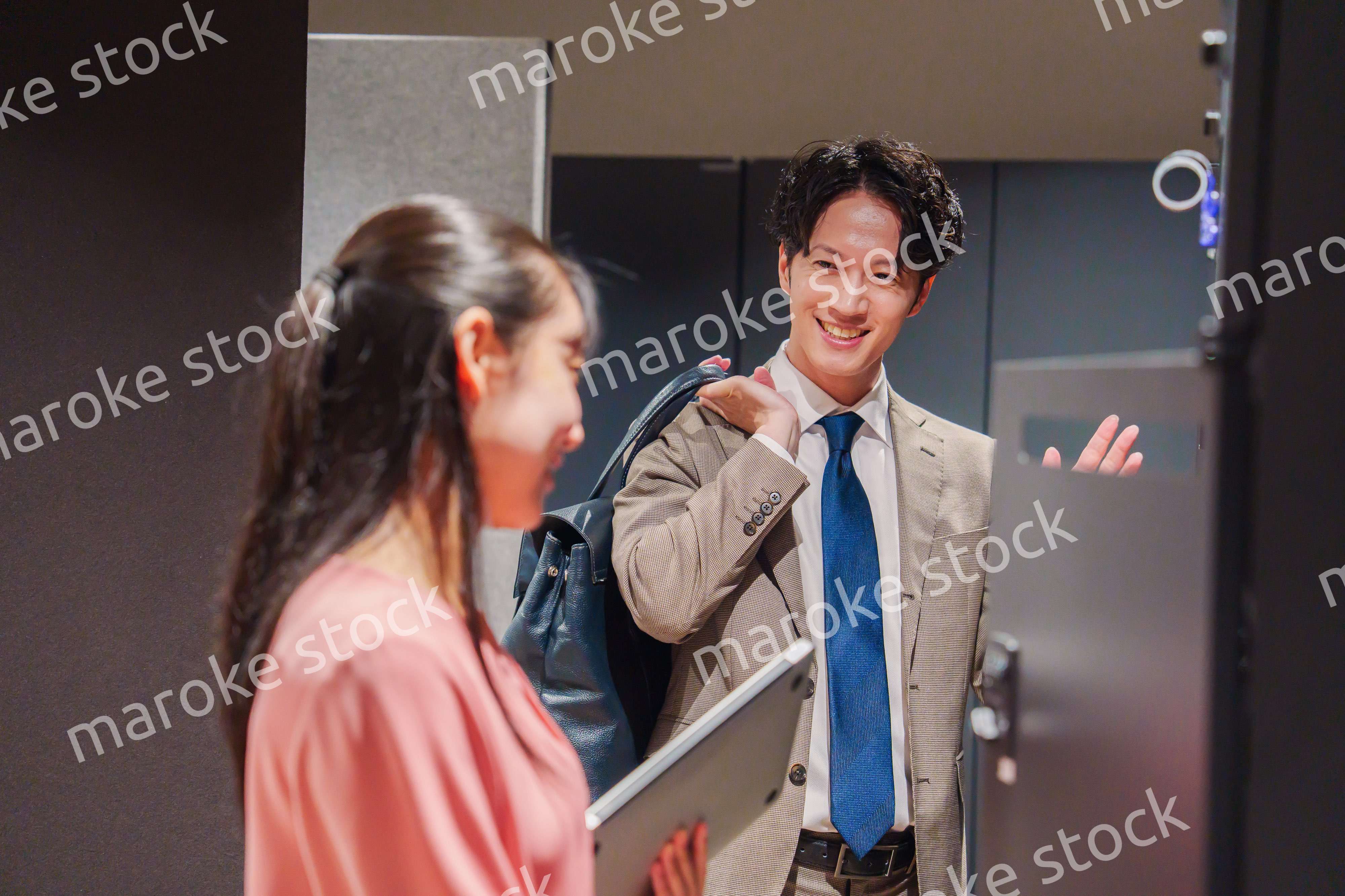 オフィスのロッカーで会話をする男女の会社員