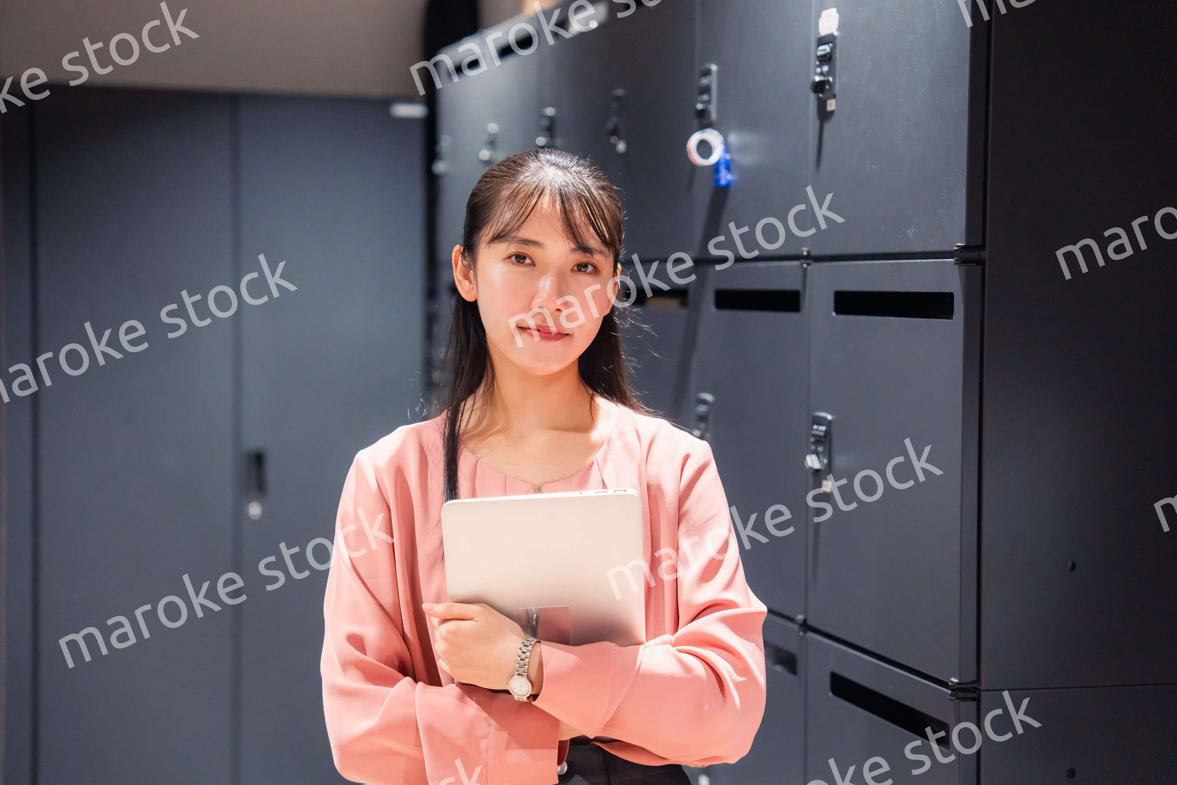 オフィスのロッカーの前でパソコンを持つ若い女性