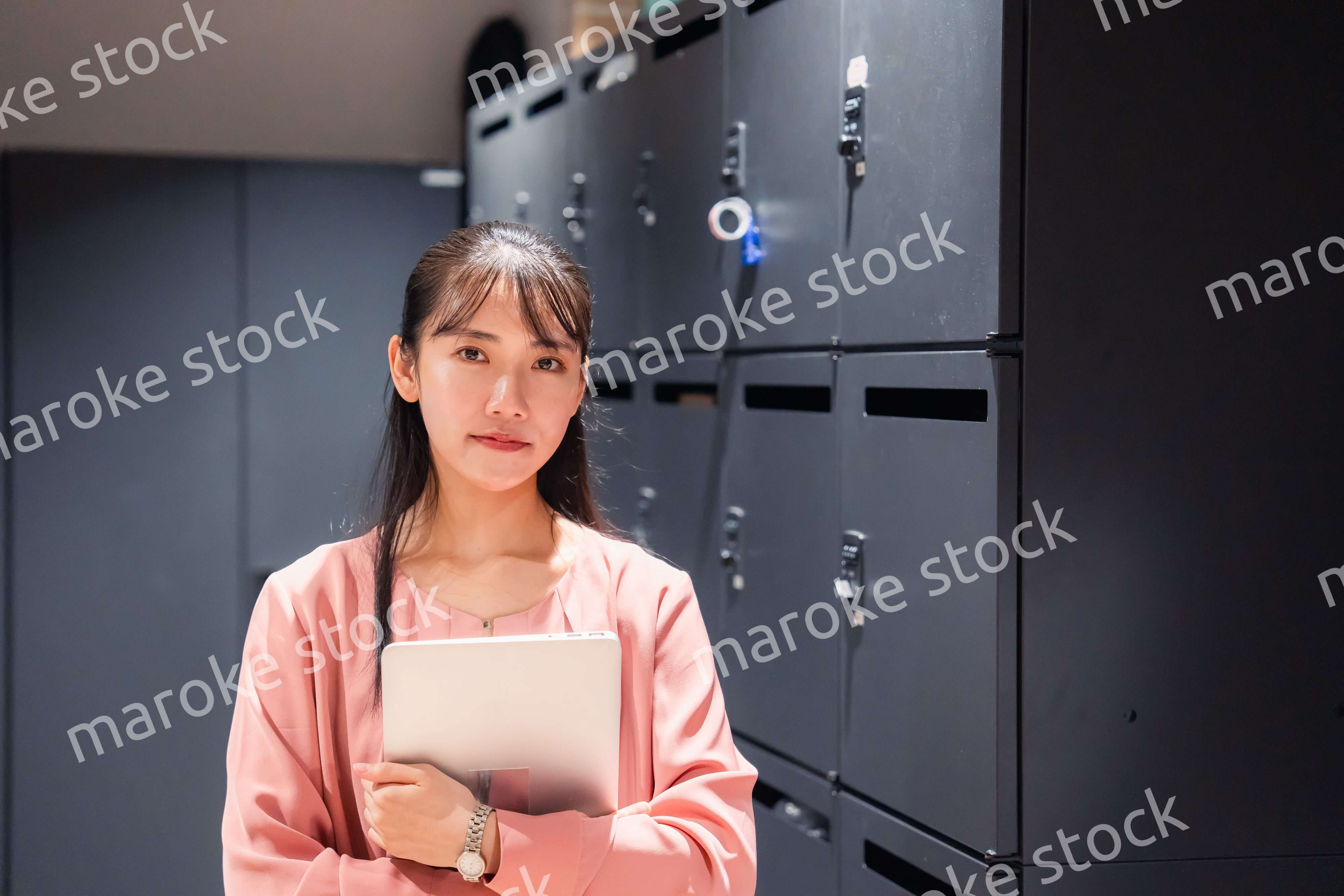 オフィスのロッカーの前でパソコンを持つ若い女性