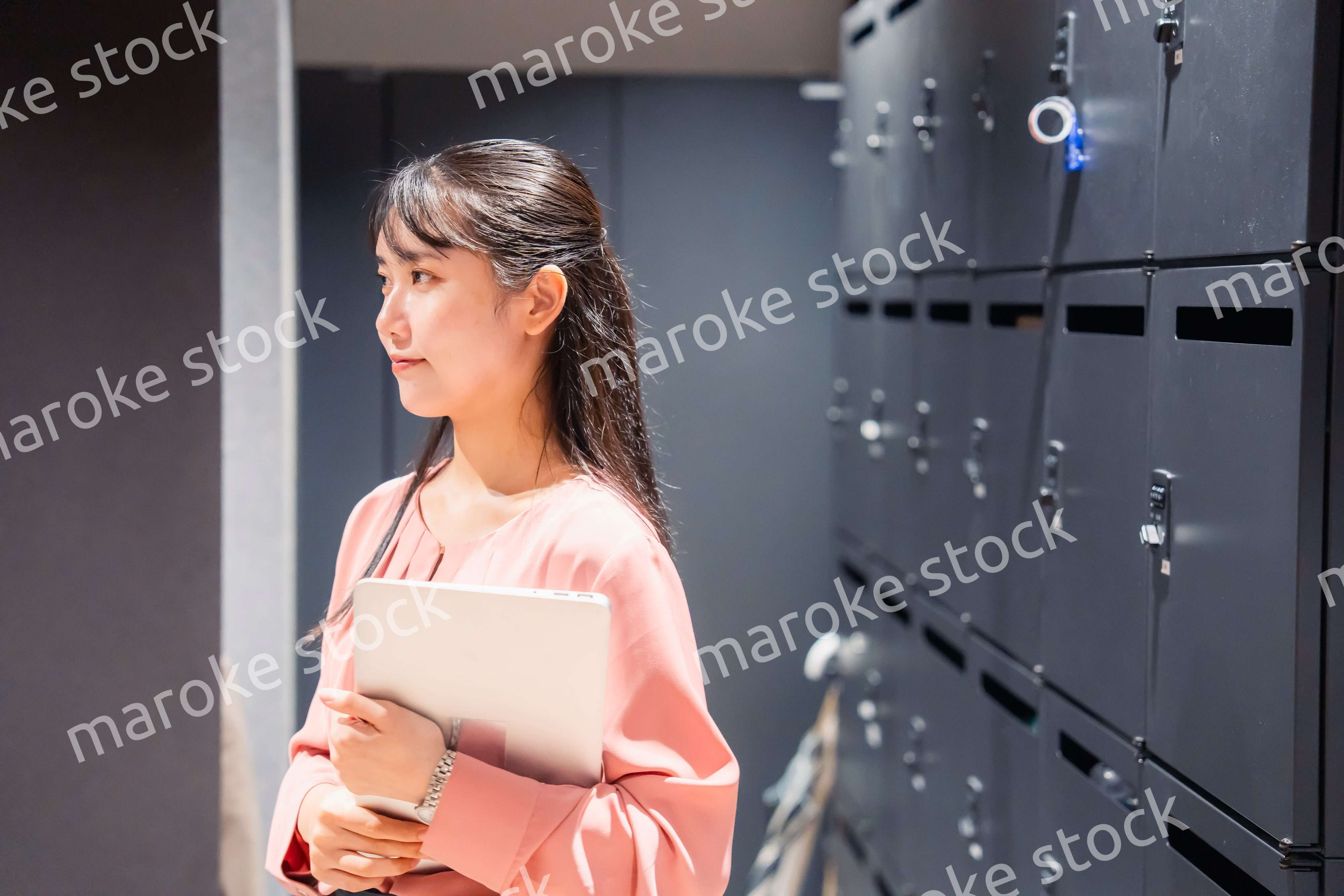 オフィスのロッカーの前でパソコンを持つ若い女性
