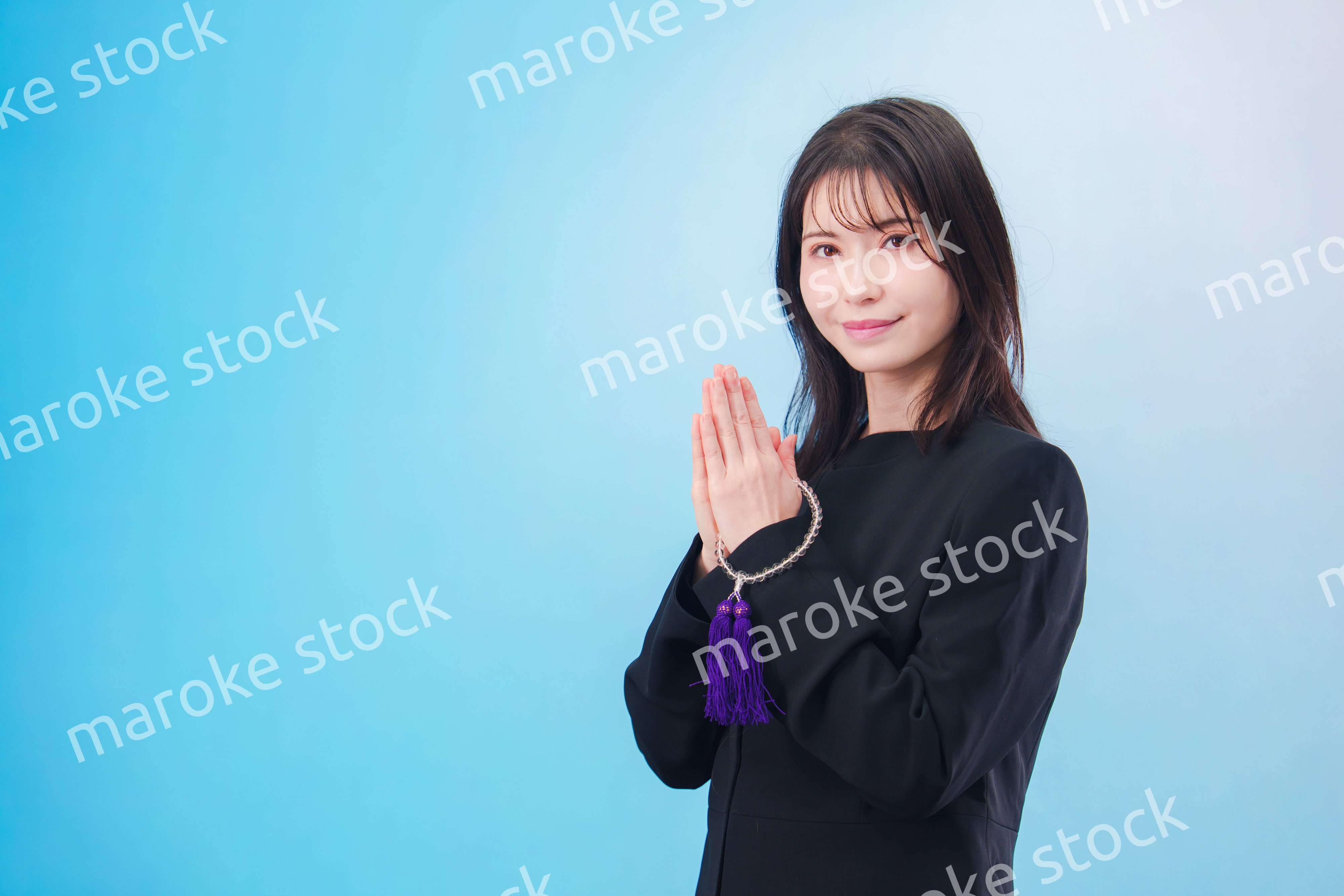 喪服を着て手を合わせる女性（水色背景）