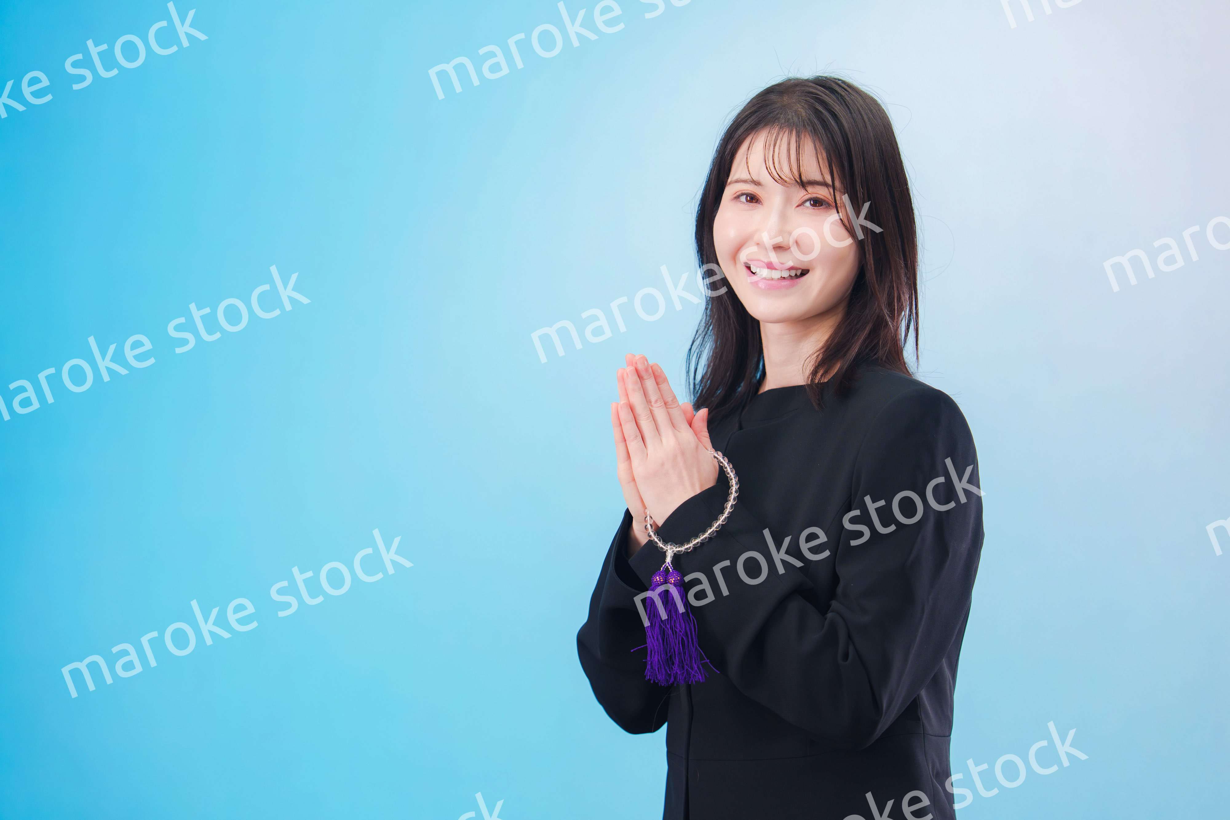 喪服を着て手を合わせる女性（水色背景）