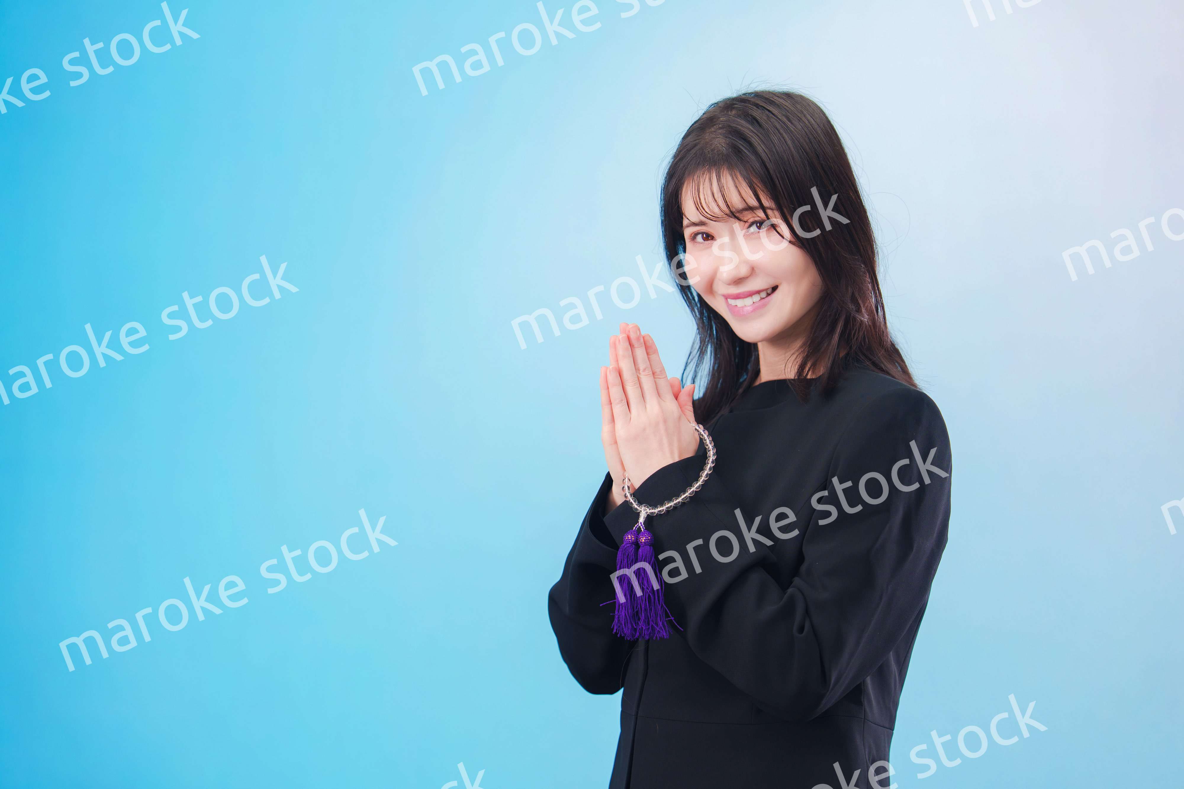 喪服を着て手を合わせる女性（水色背景）