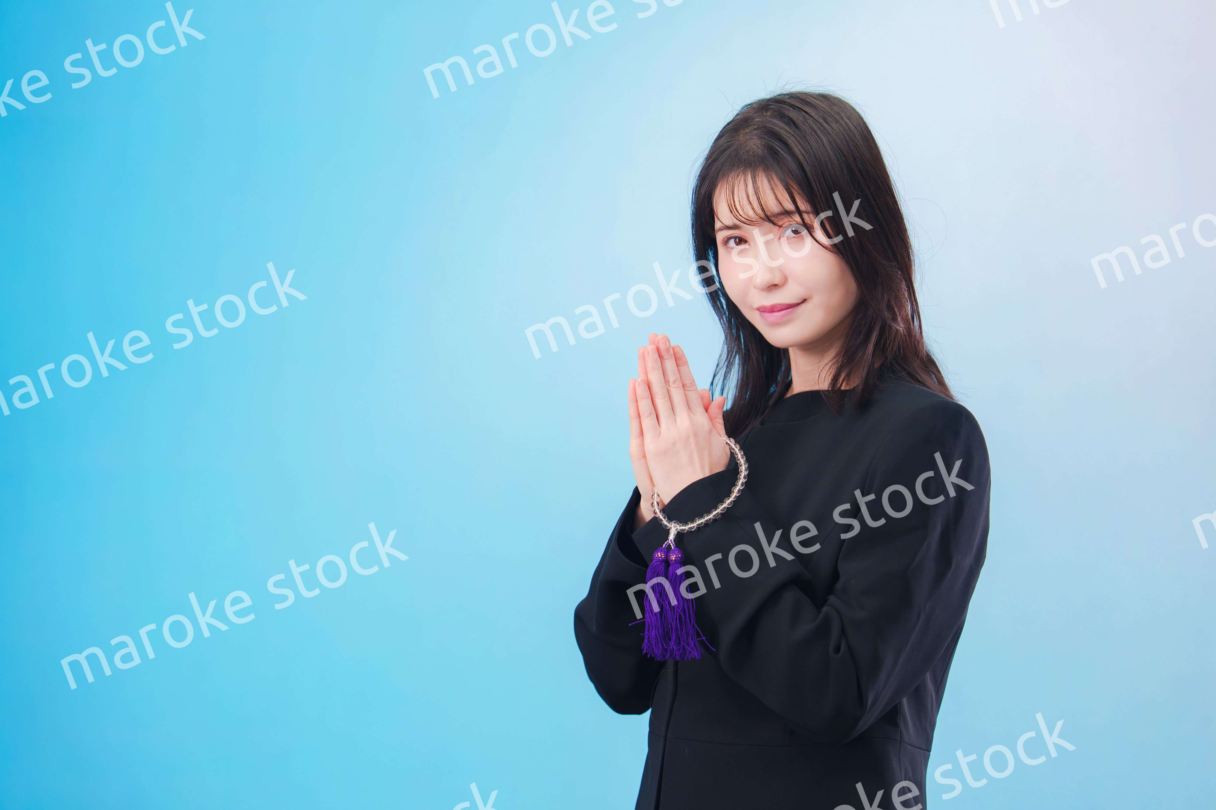 喪服を着て手を合わせる女性（水色背景）