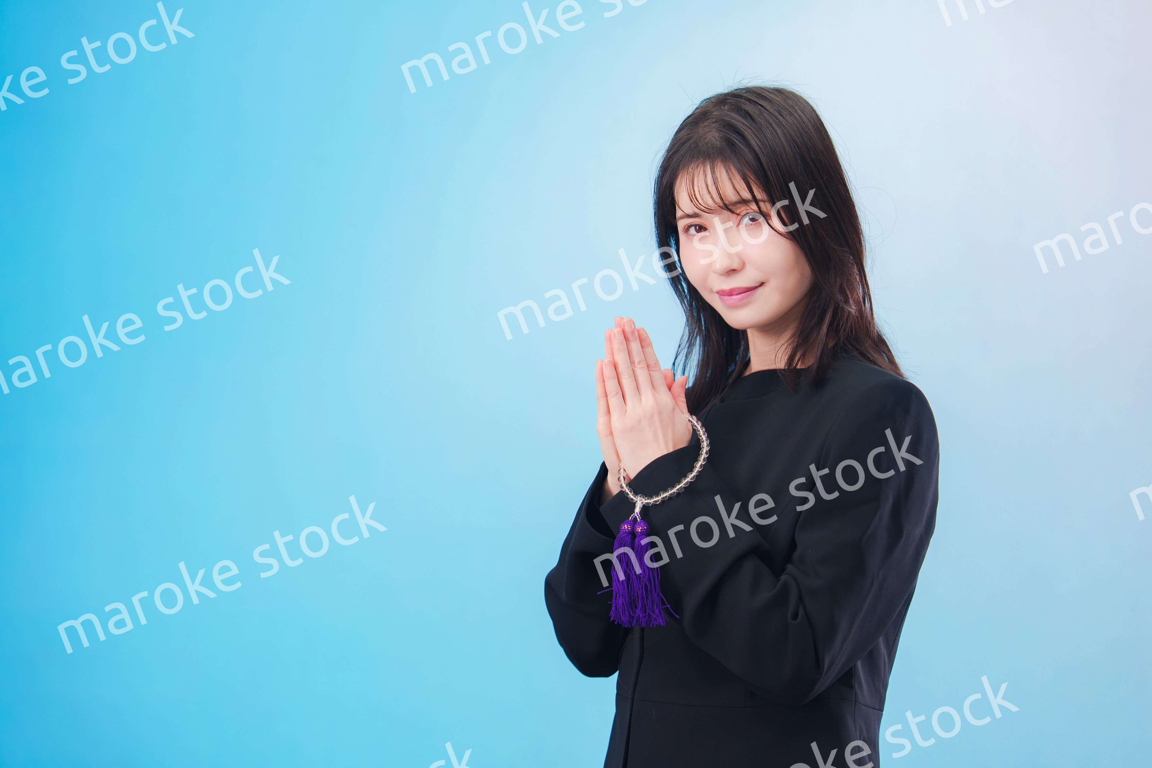 喪服を着て手を合わせる女性（水色背景）