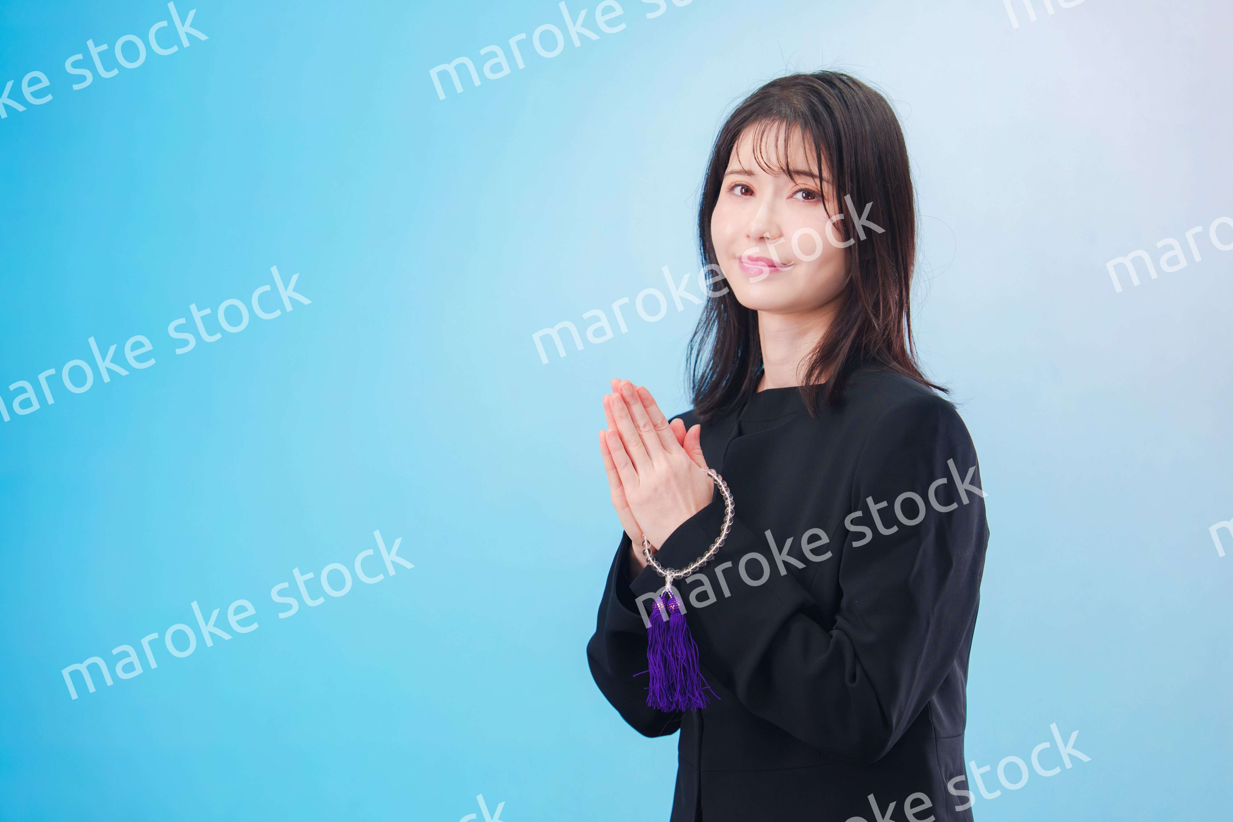 喪服を着て手を合わせる女性（水色背景）