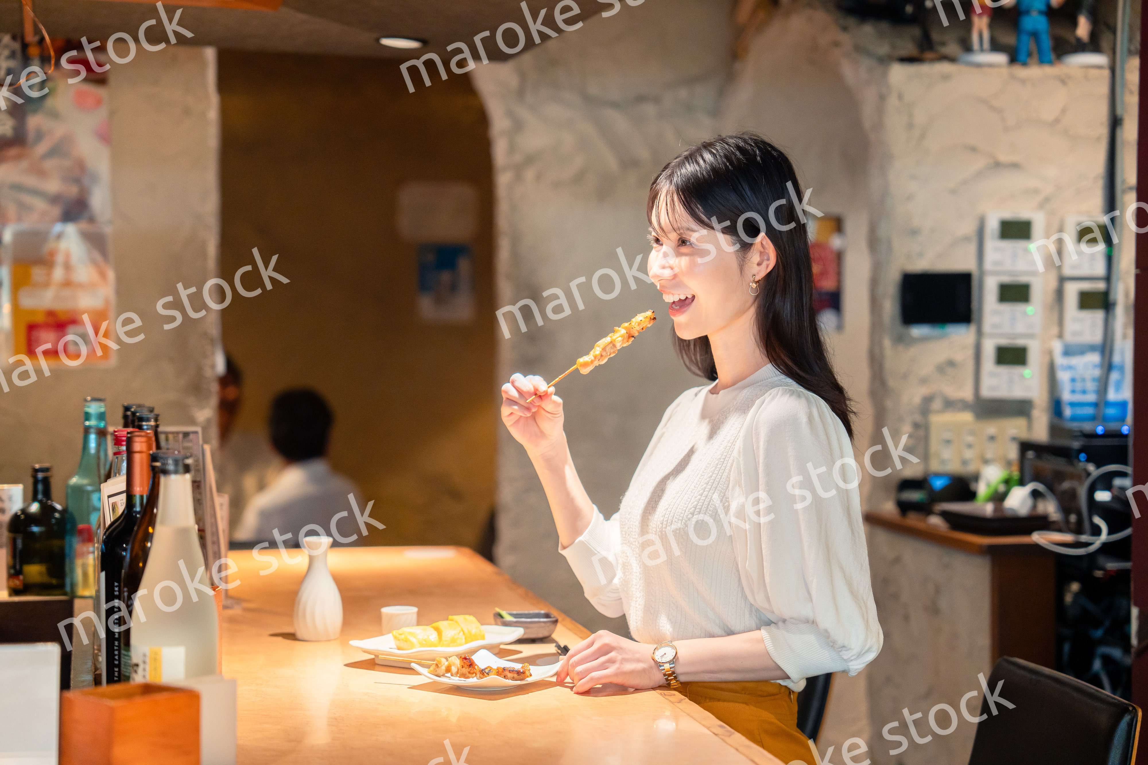 一人でカウンター席に座って焼き鳥を食べる女性