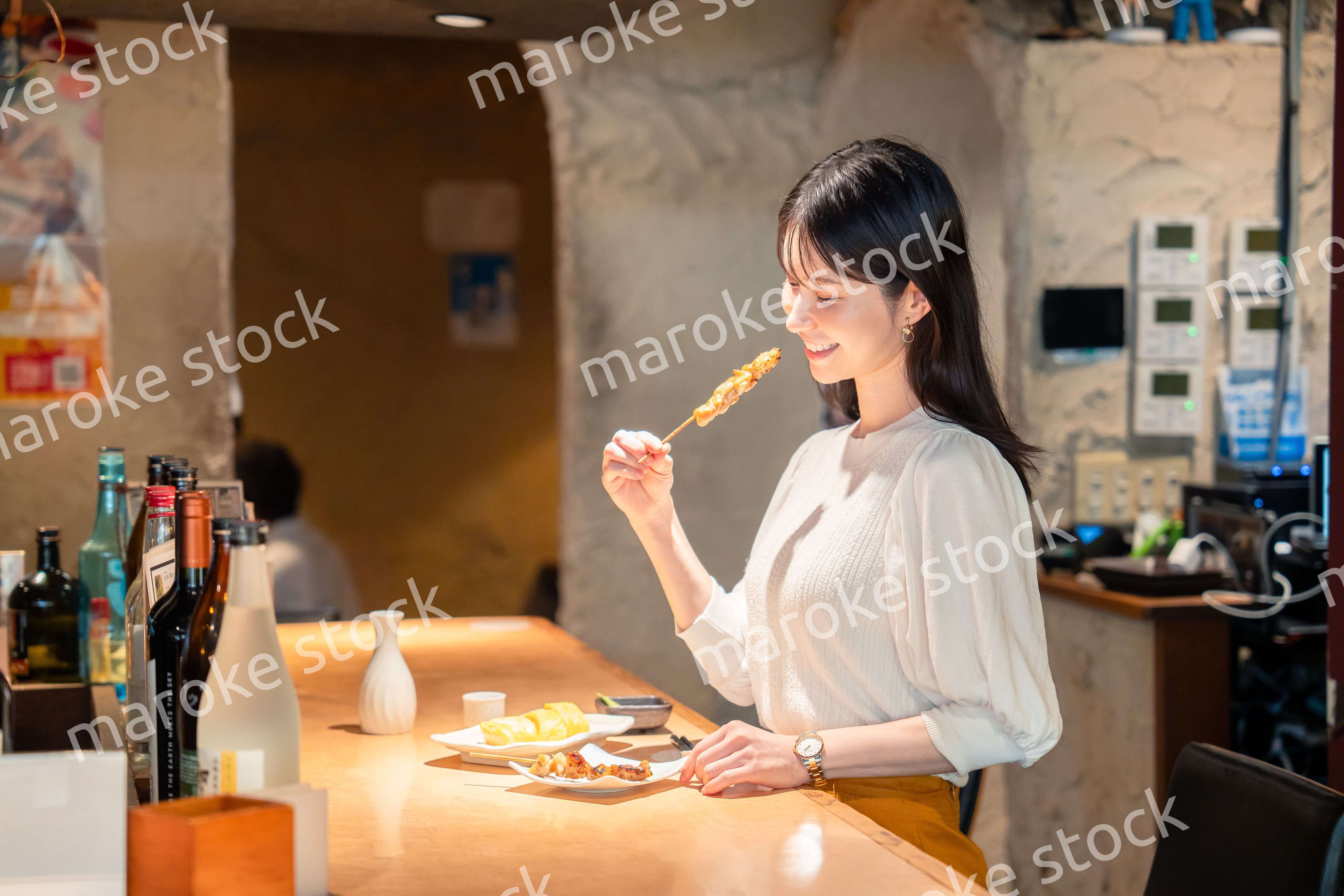 一人でカウンター席に座って焼き鳥を食べる女性
