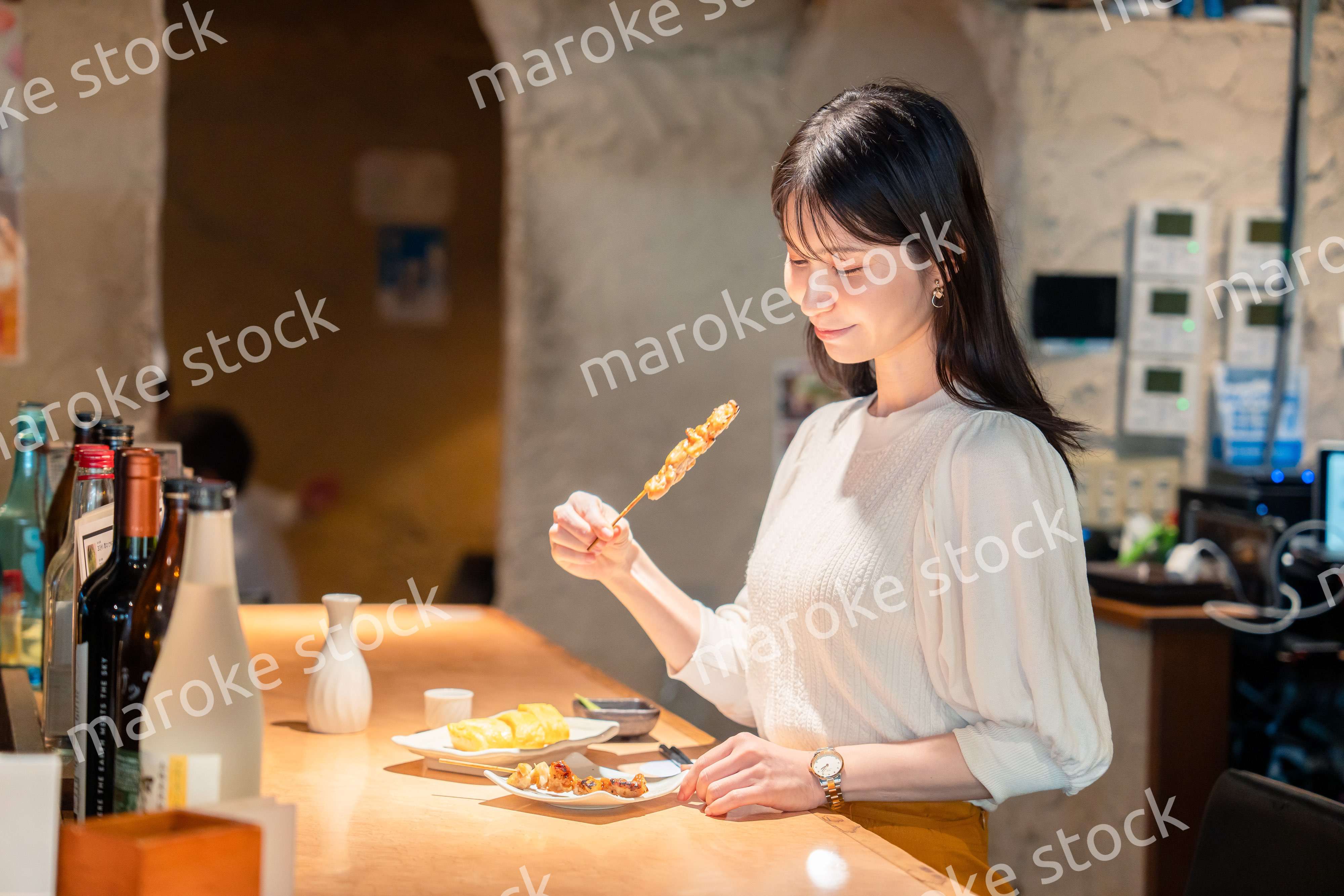 一人でカウンター席に座って焼き鳥を食べる女性