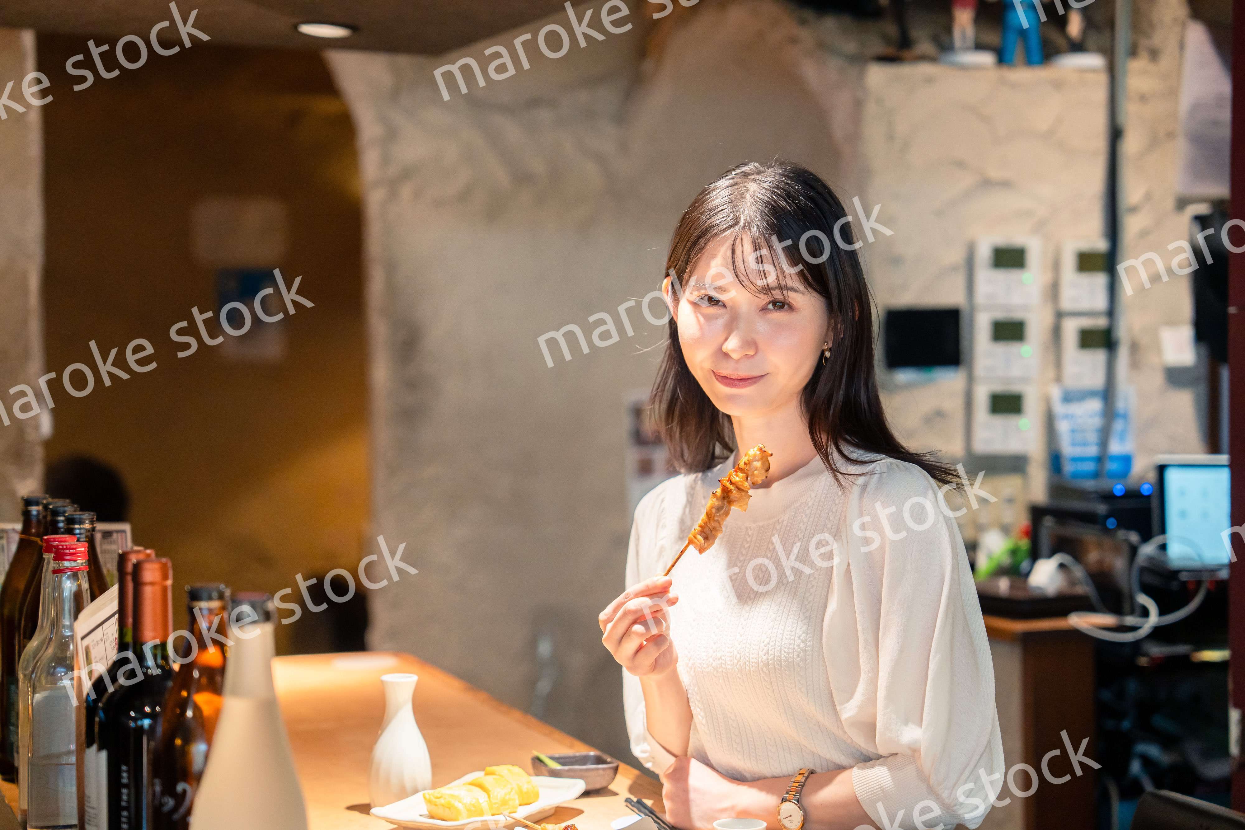 一人でカウンター席に座って焼き鳥を食べる女性