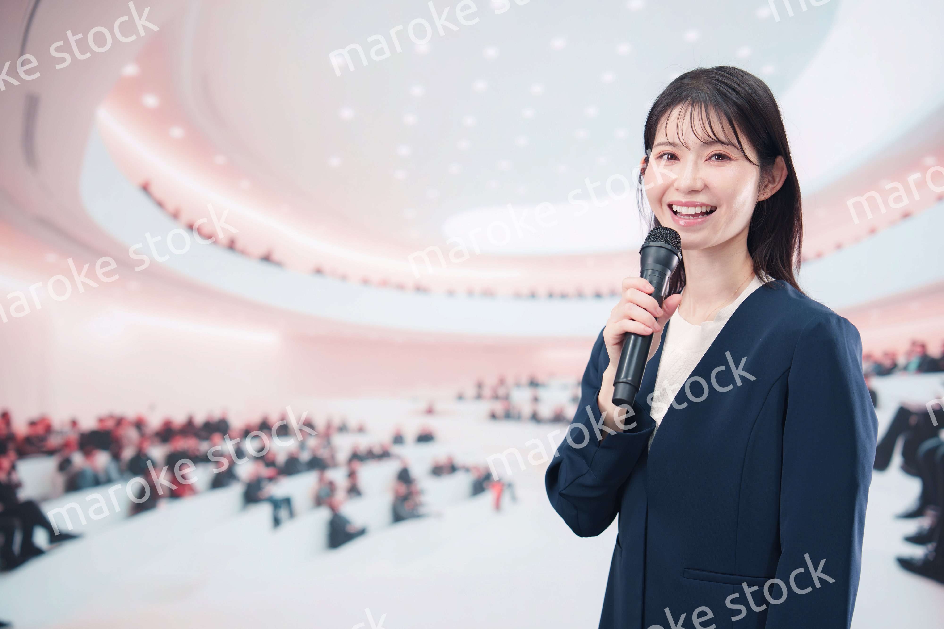 ホールで司会・プレゼンをするスーツを着た若い女性