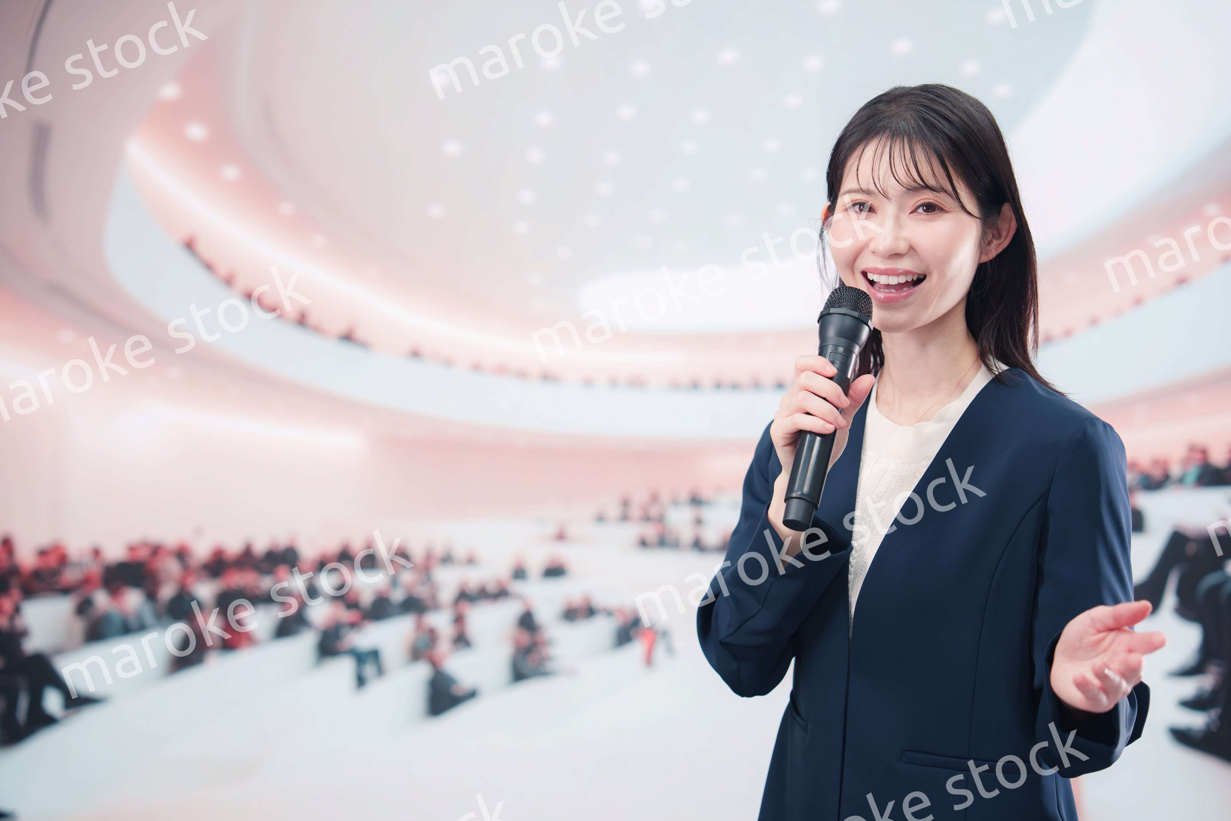 ホールで司会・プレゼンをするスーツを着た若い女性
