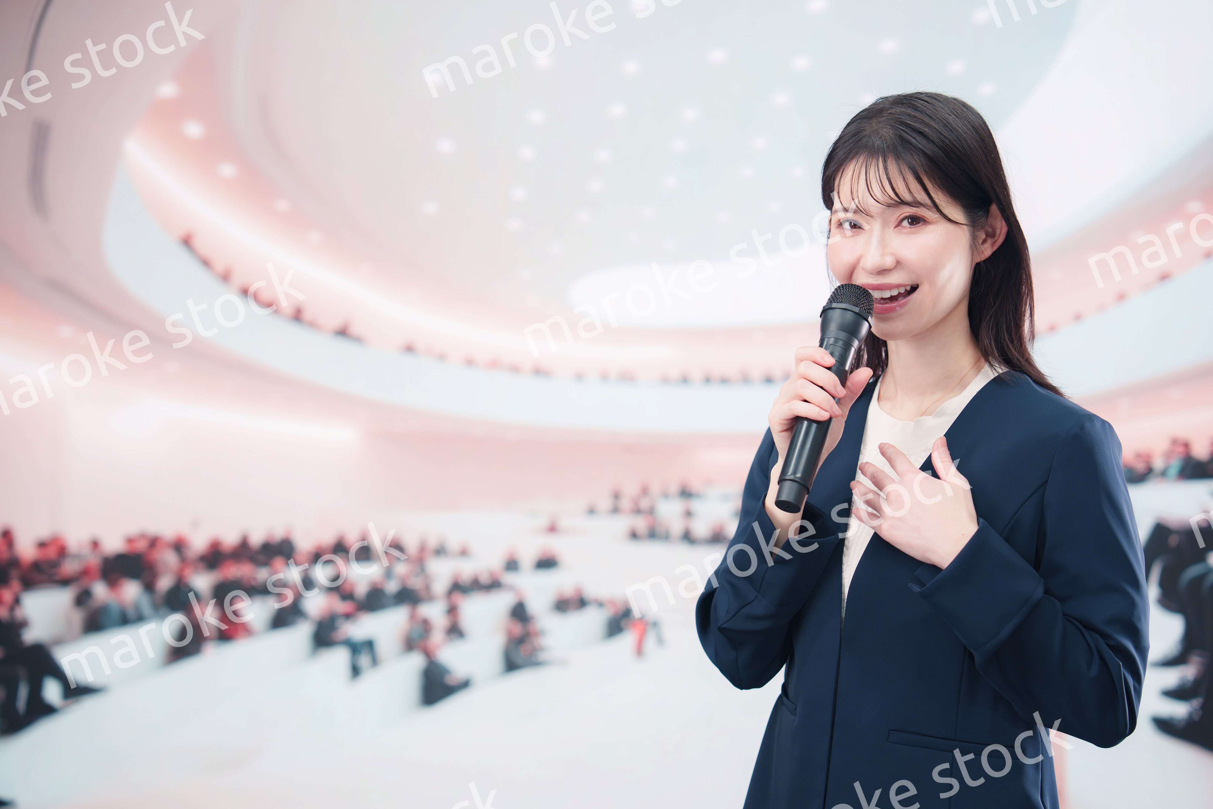 ホールで司会・プレゼンをするスーツを着た若い女性