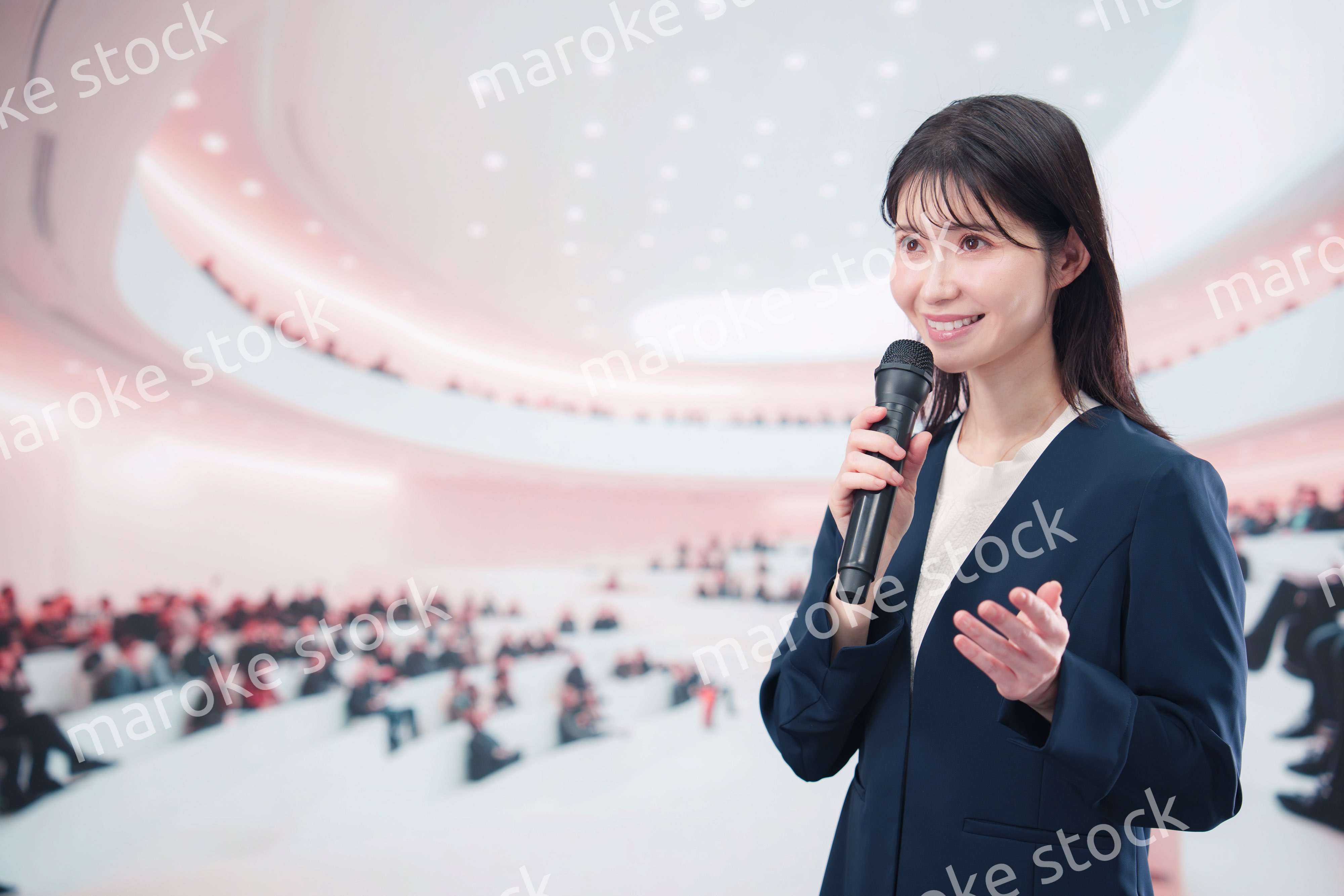 ホールで司会・プレゼンをするスーツを着た若い女性