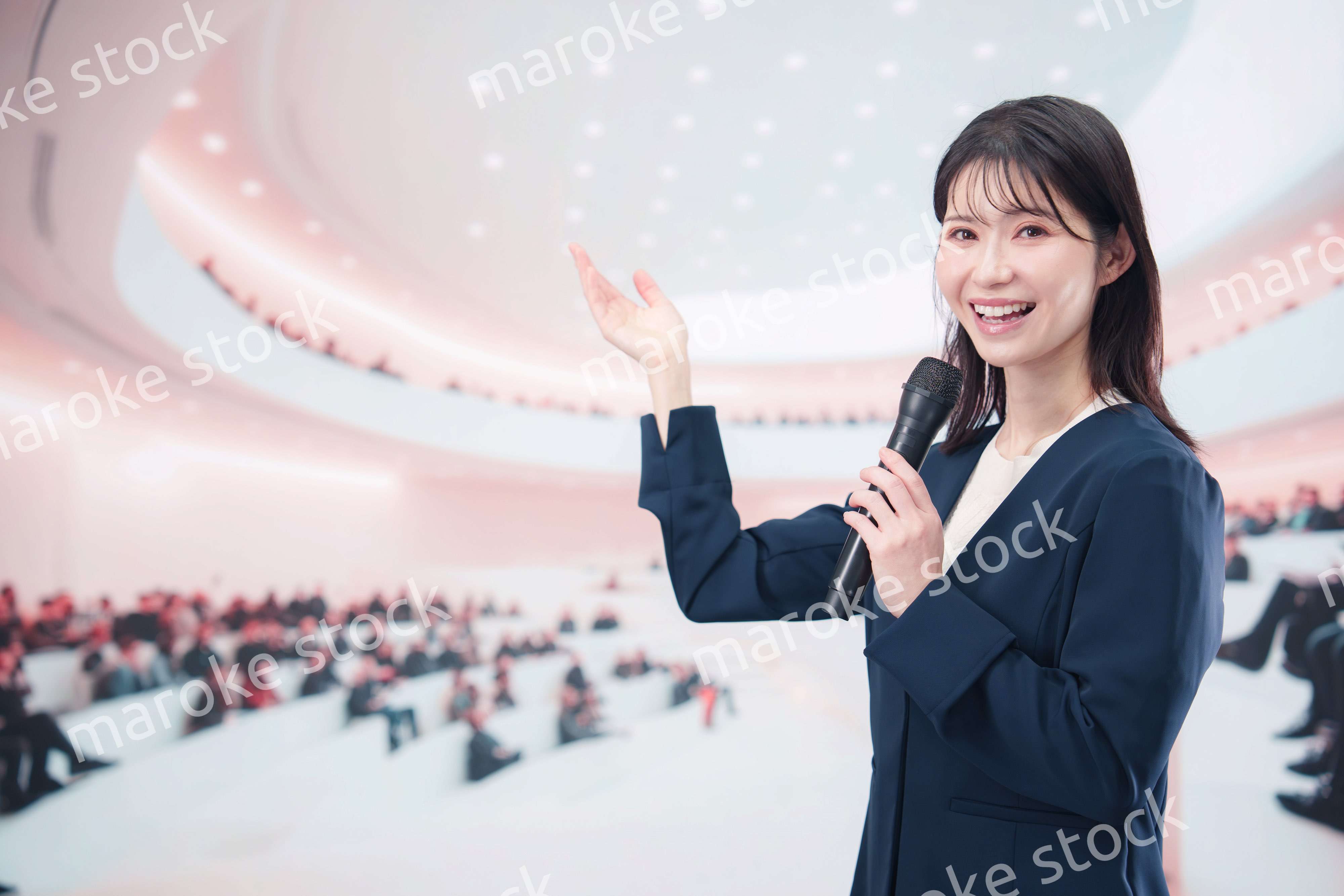 ホールで司会・プレゼンをするスーツを着た若い女性