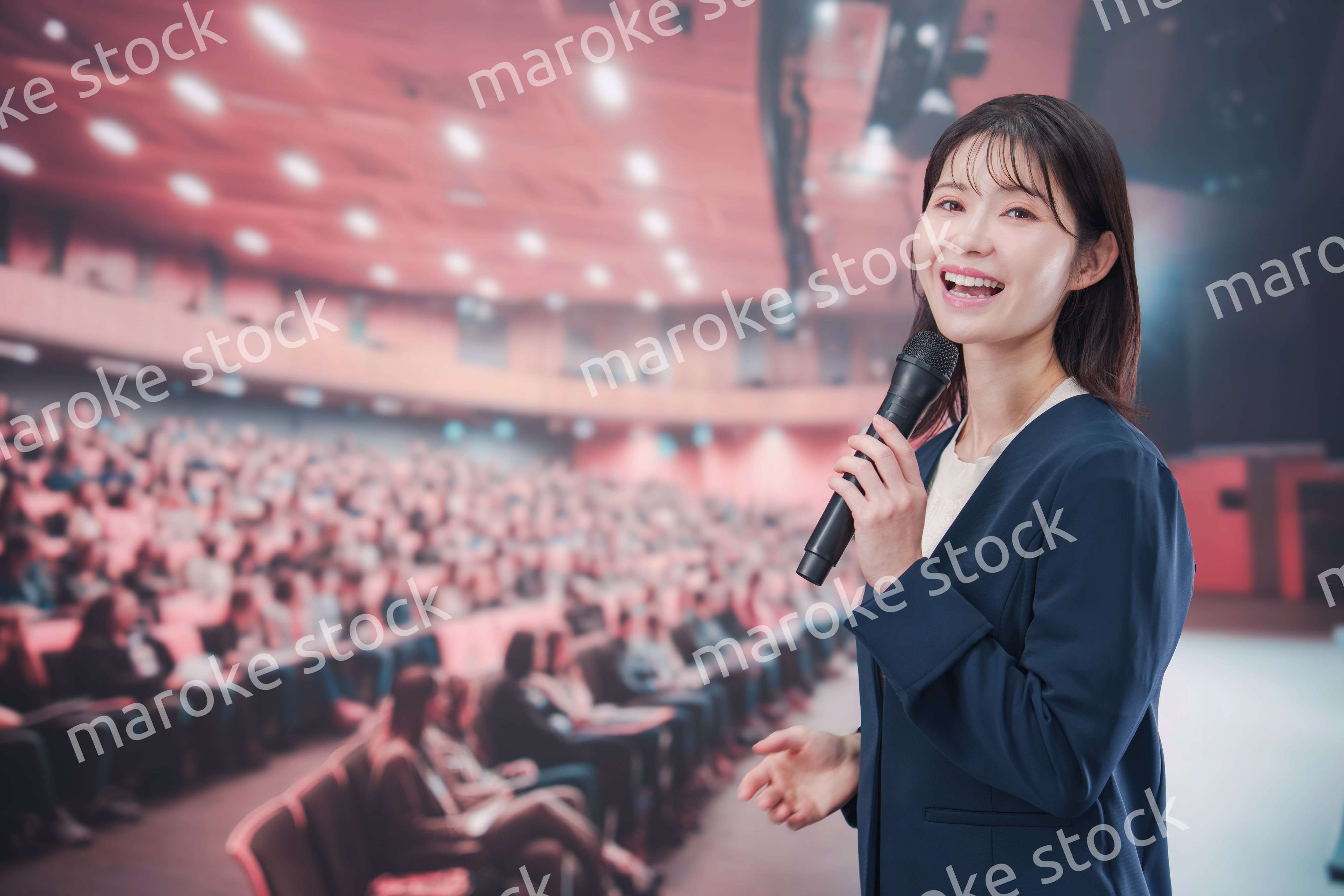 大勢の聴衆が集まるホールで司会をする若い女性