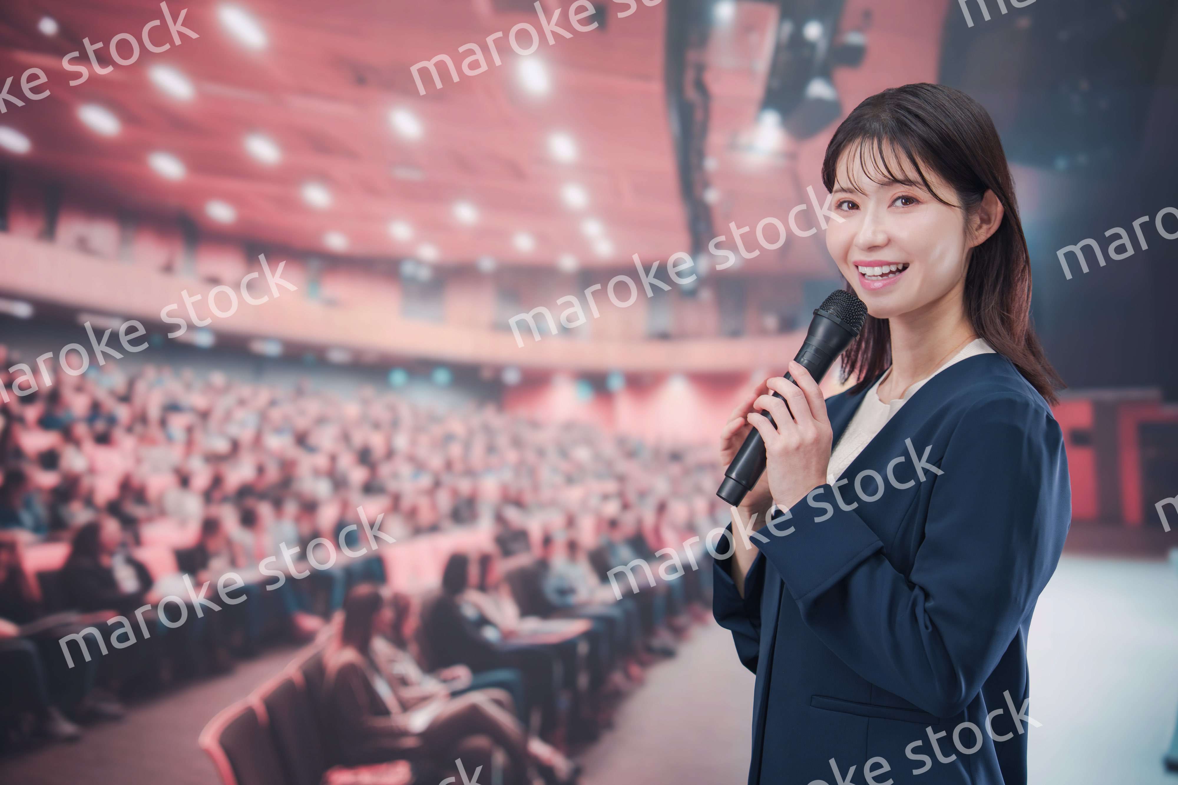 大勢の聴衆が集まるホールで司会をする若い女性