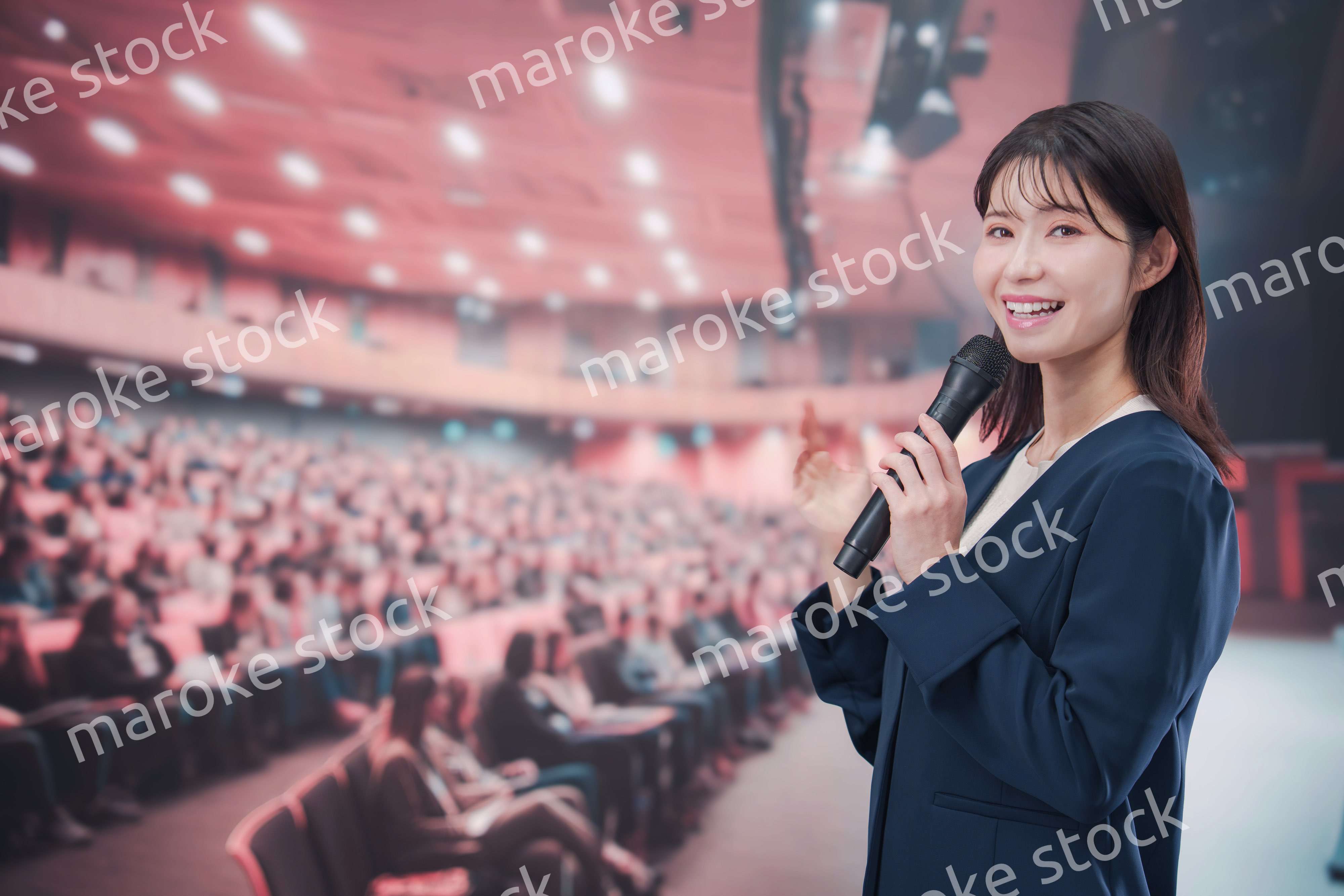大勢の聴衆が集まるホールで司会をする若い女性