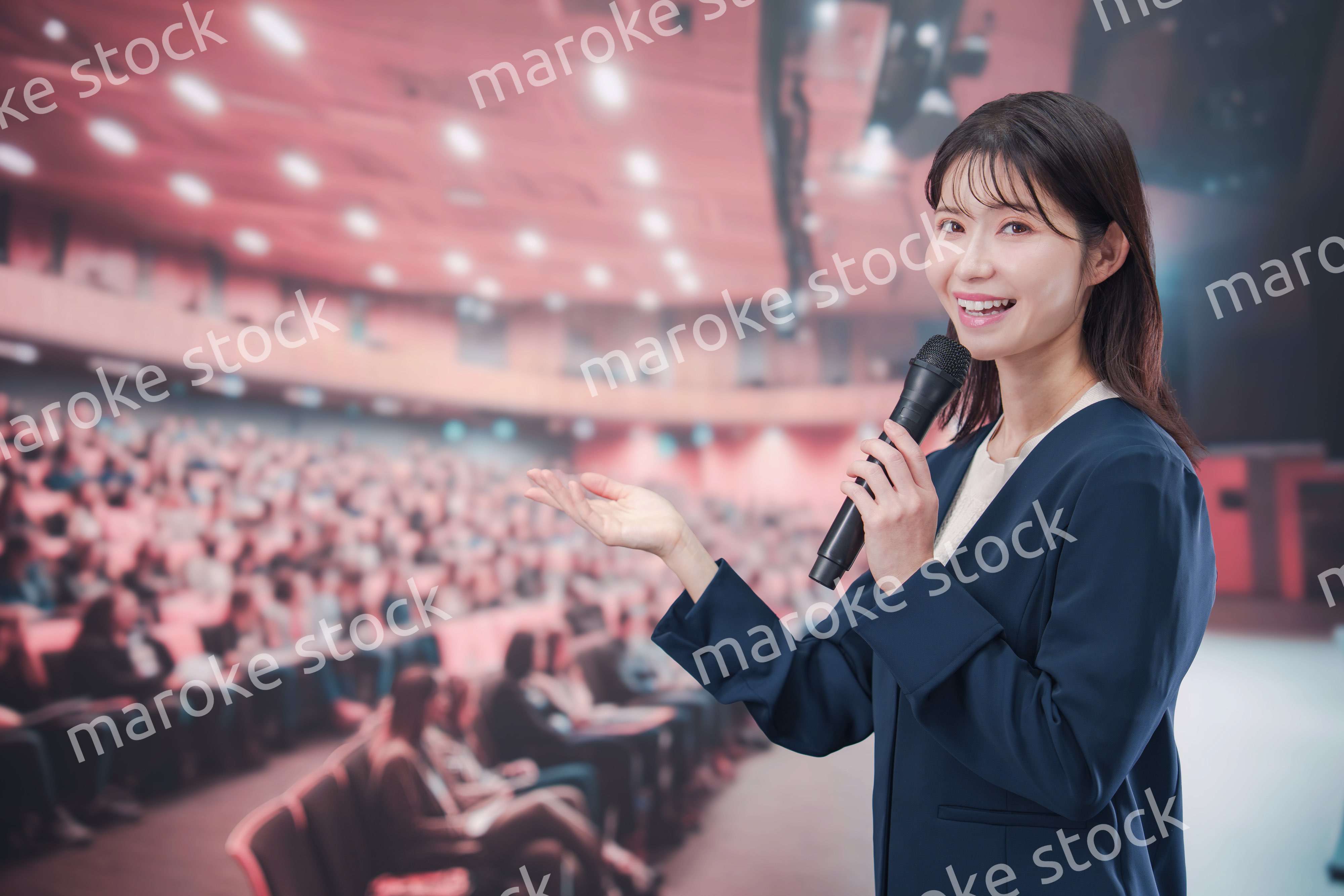 大勢の聴衆が集まるホールで司会をする若い女性