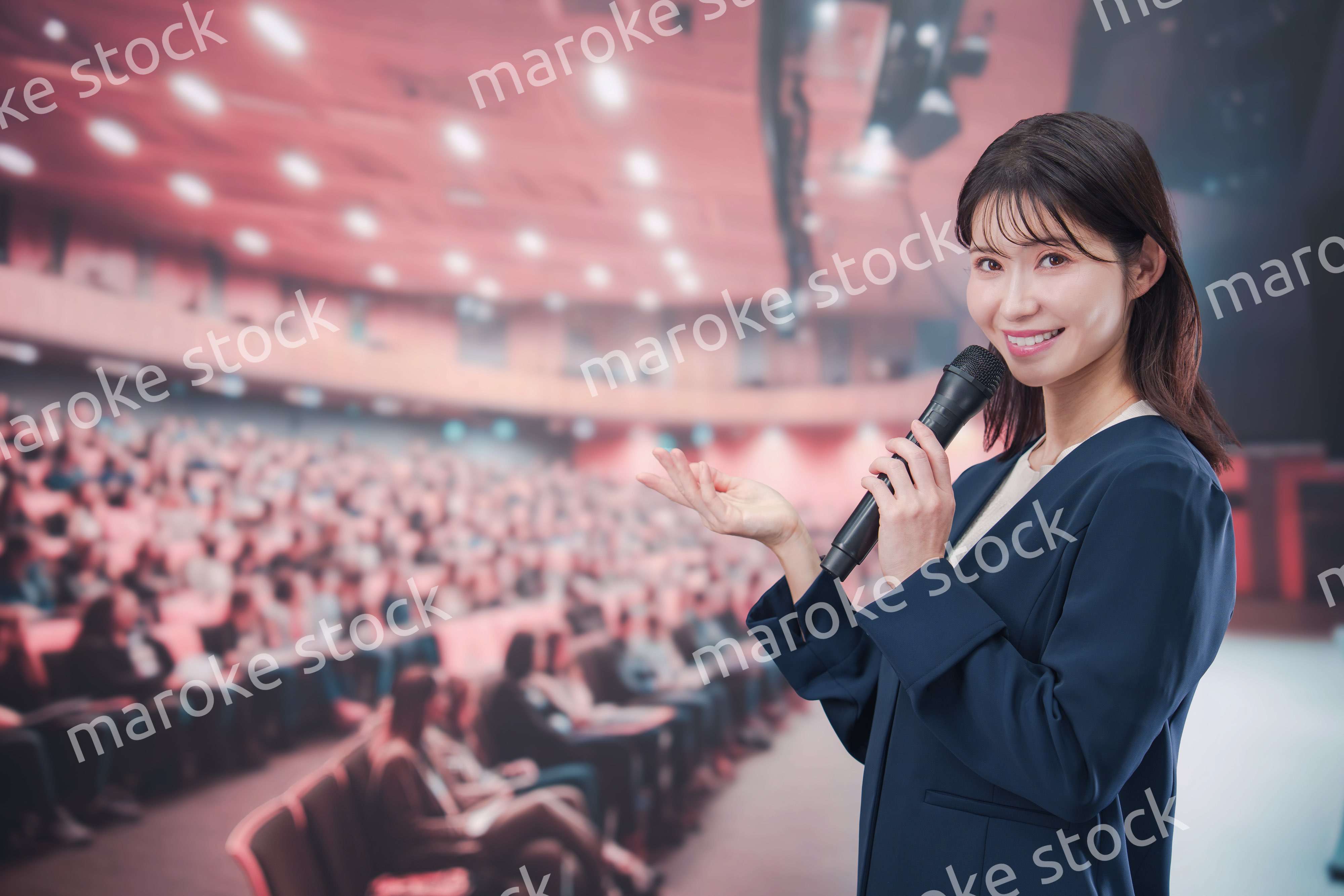 大勢の聴衆が集まるホールで司会をする若い女性