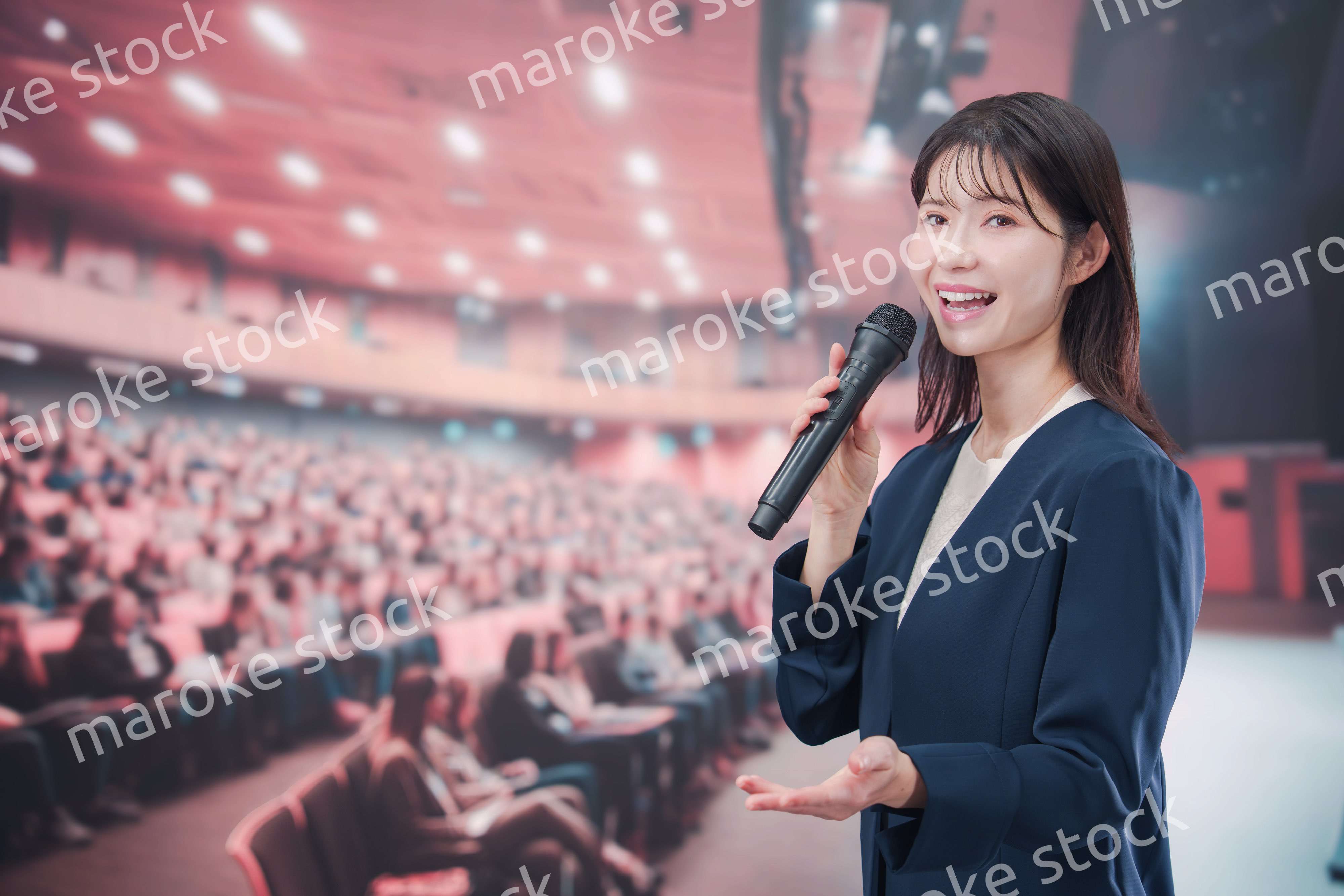 大勢の聴衆が集まるホールで司会をする若い女性