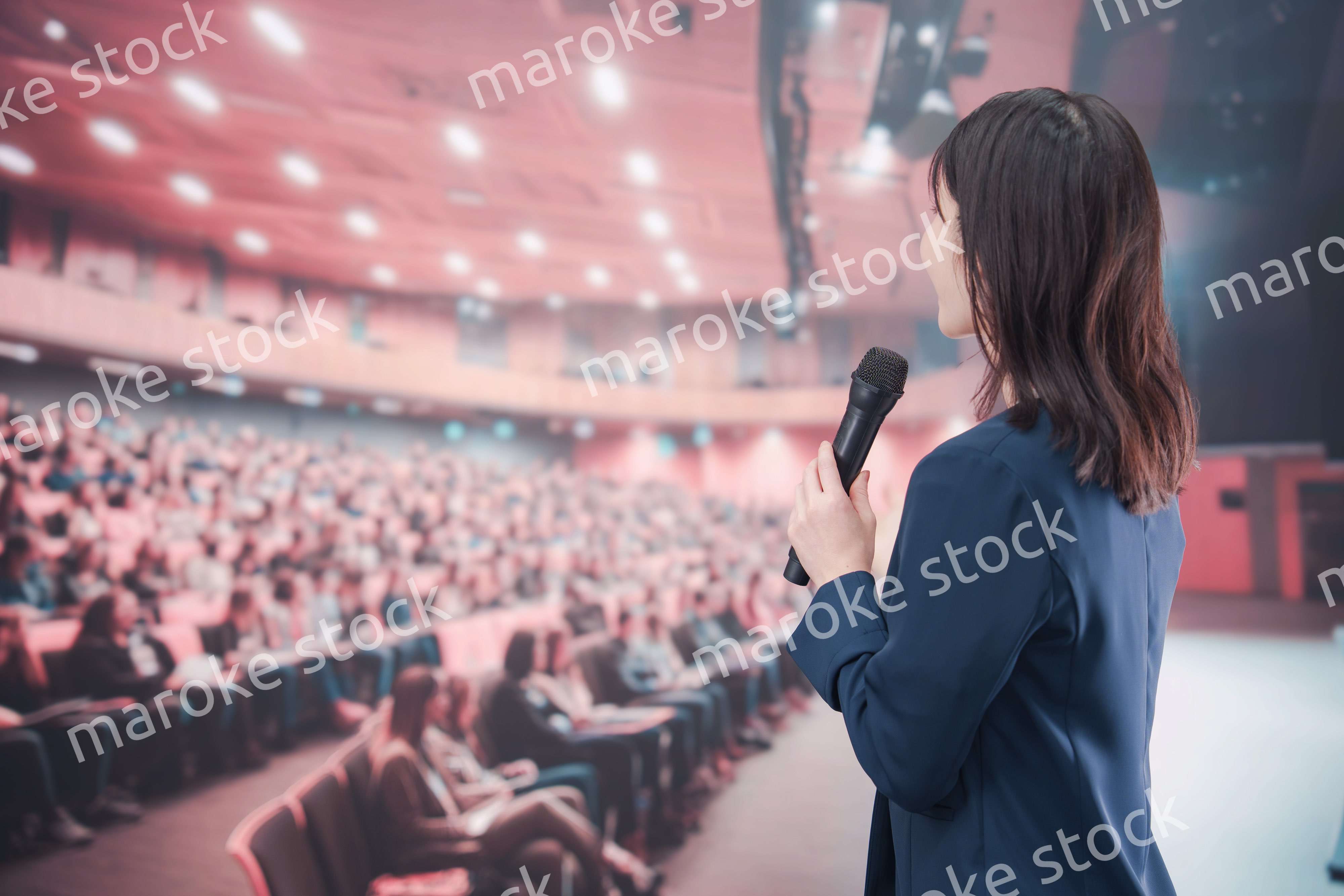大勢の聴衆が集まるホールで司会をする若い女性