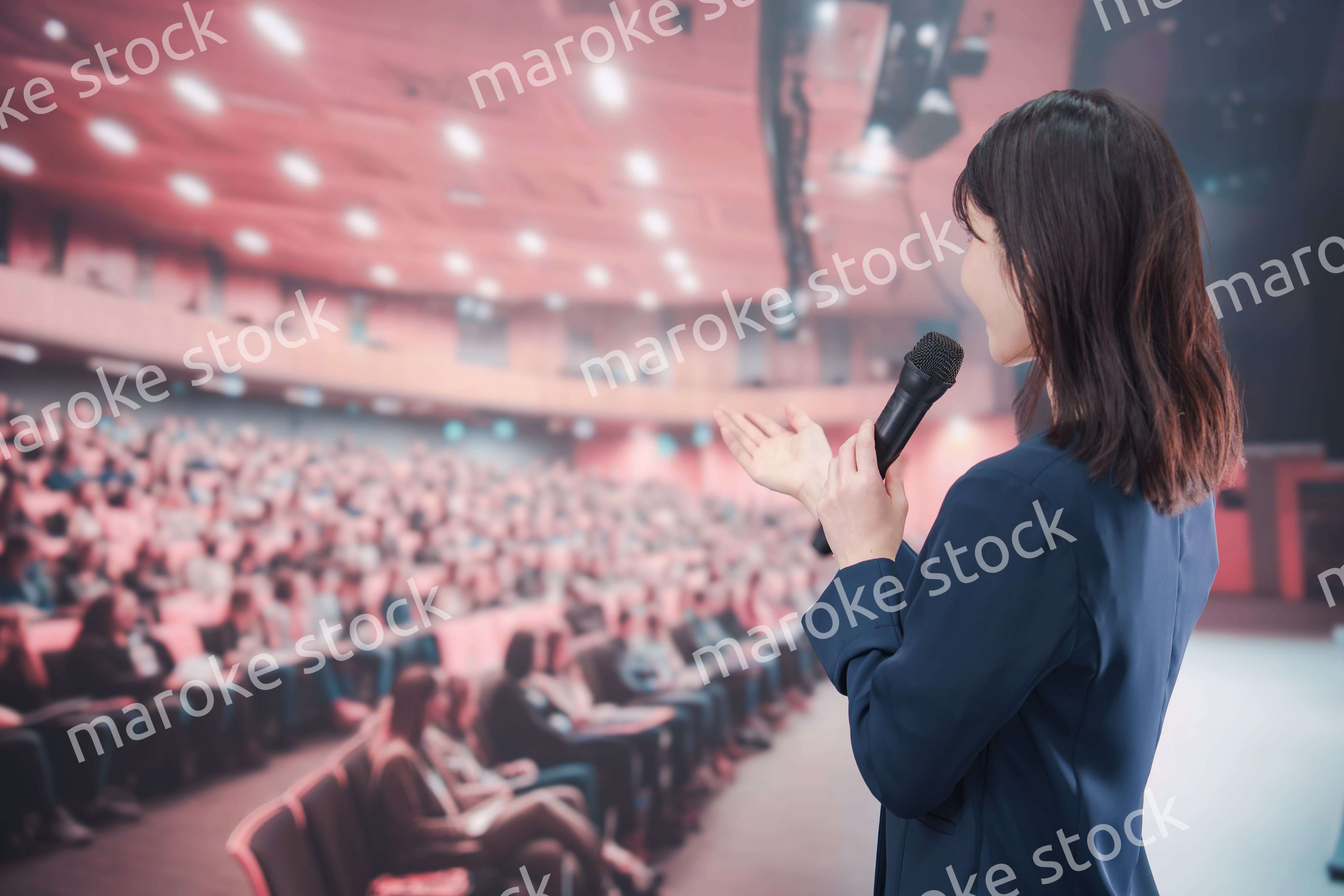 大勢の聴衆が集まるホールで司会をする若い女性