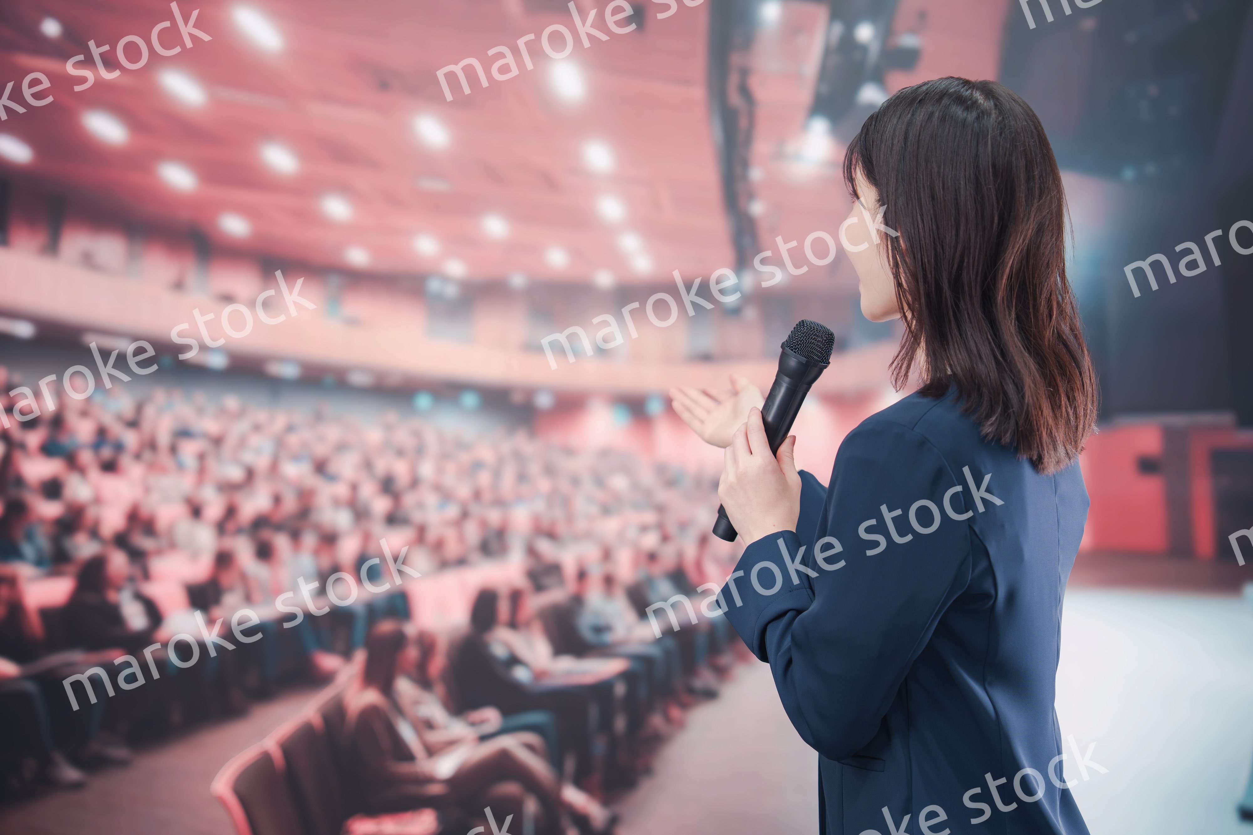 大勢の聴衆が集まるホールで司会をする若い女性