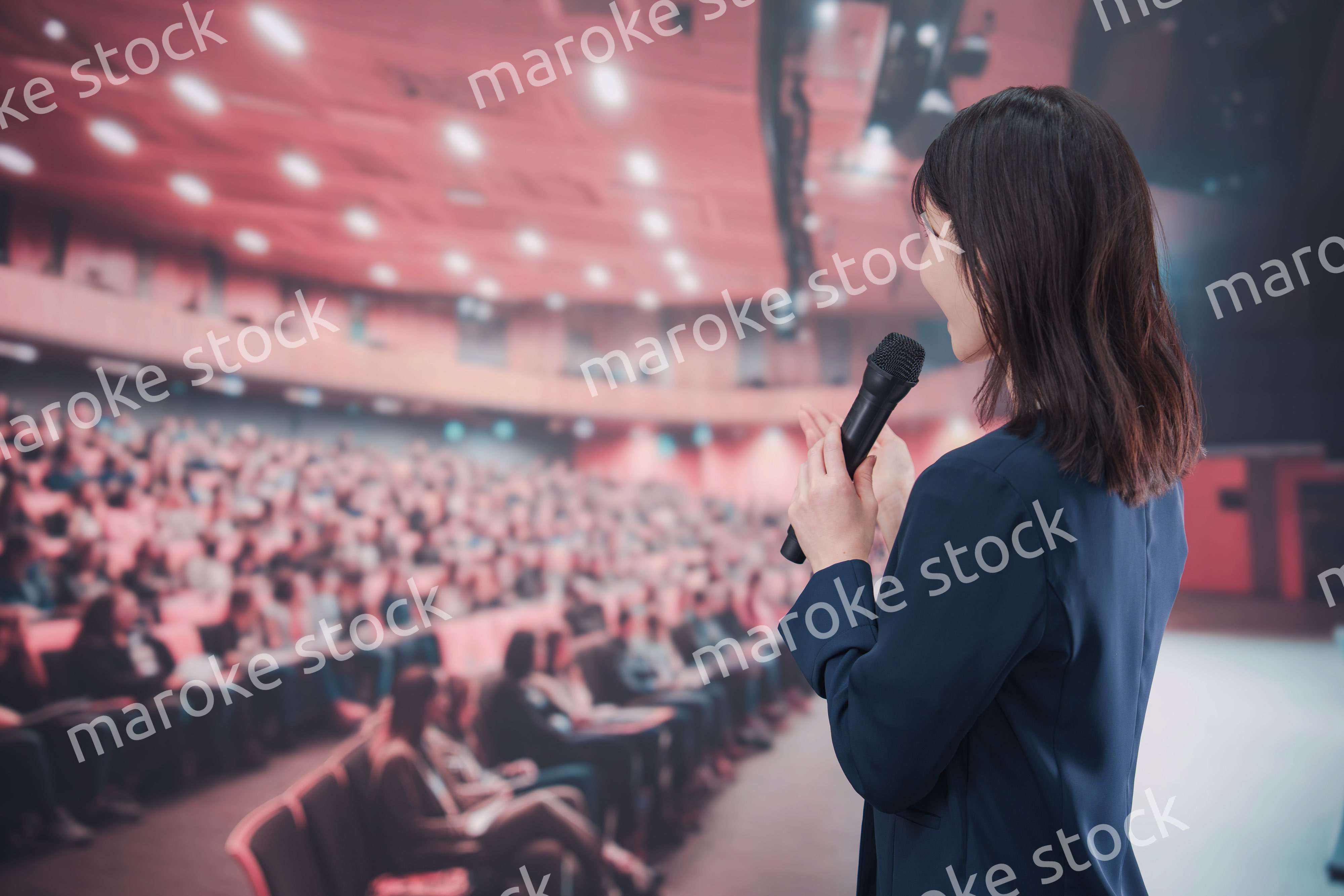 大勢の聴衆が集まるホールで司会をする若い女性