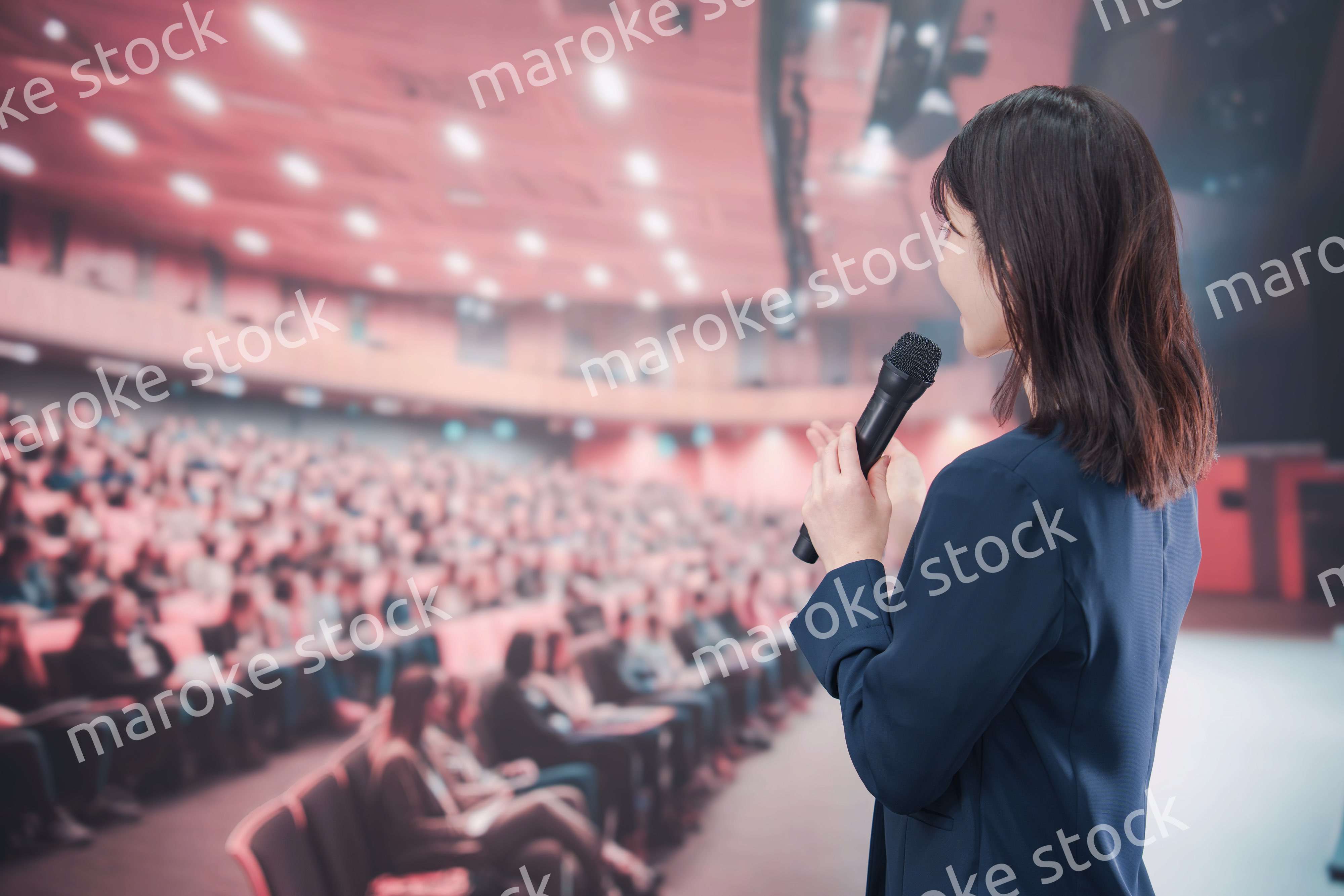 大勢の聴衆が集まるホールで司会をする若い女性