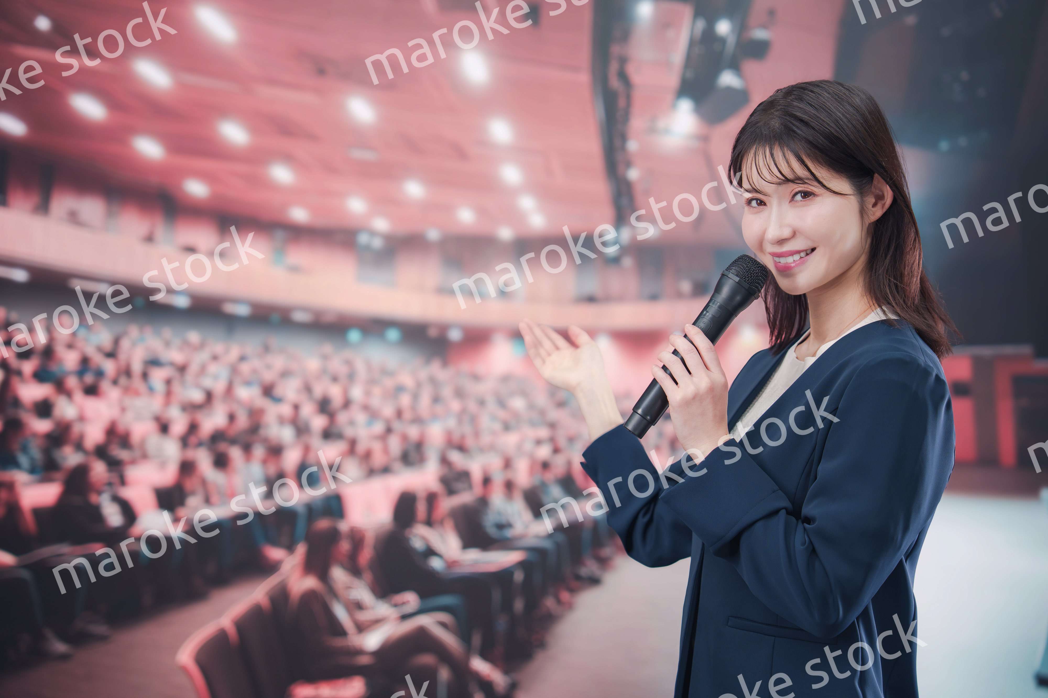 大勢の聴衆が集まるホールで司会をする若い女性
