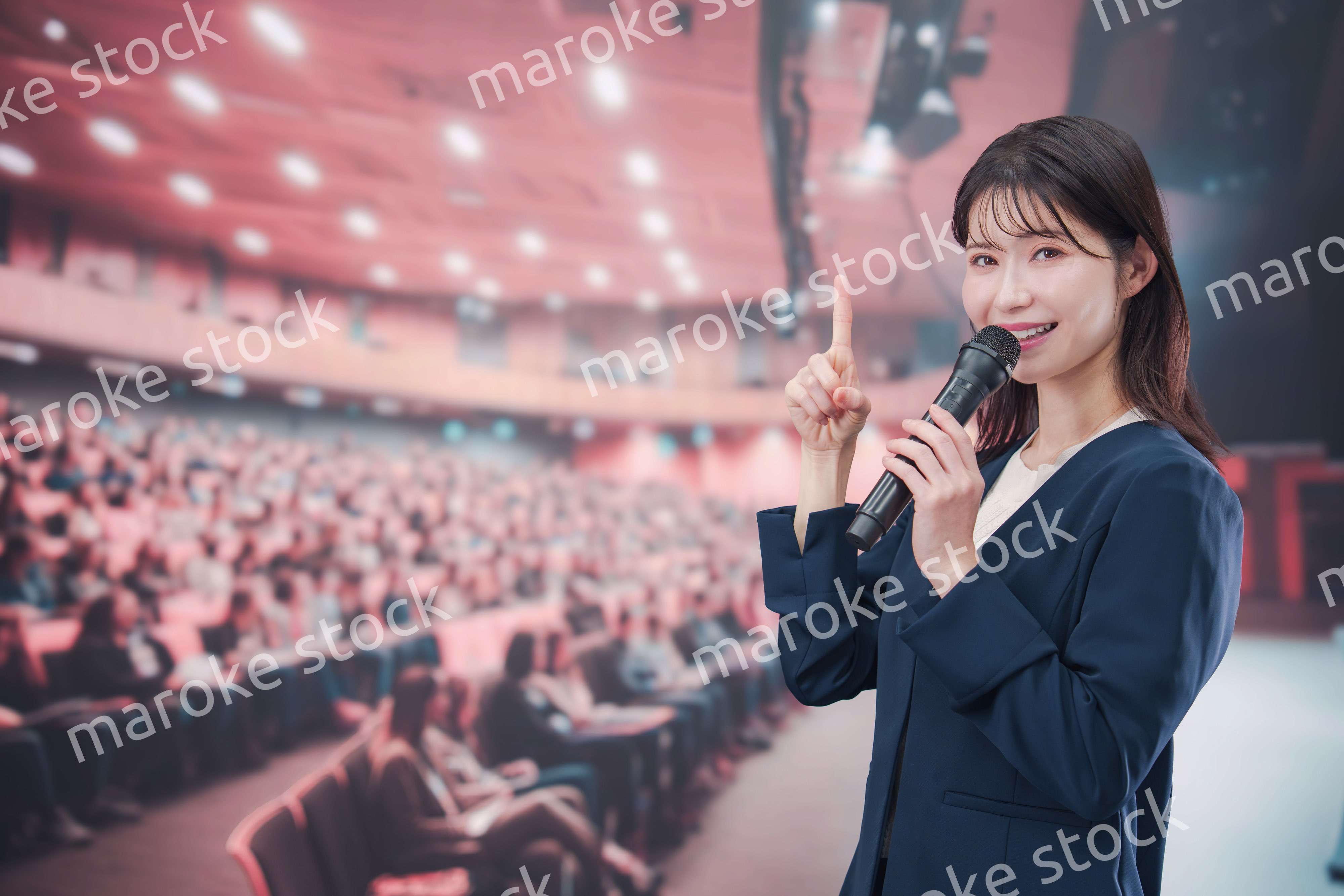 大勢の聴衆が集まるホールで司会をする若い女性
