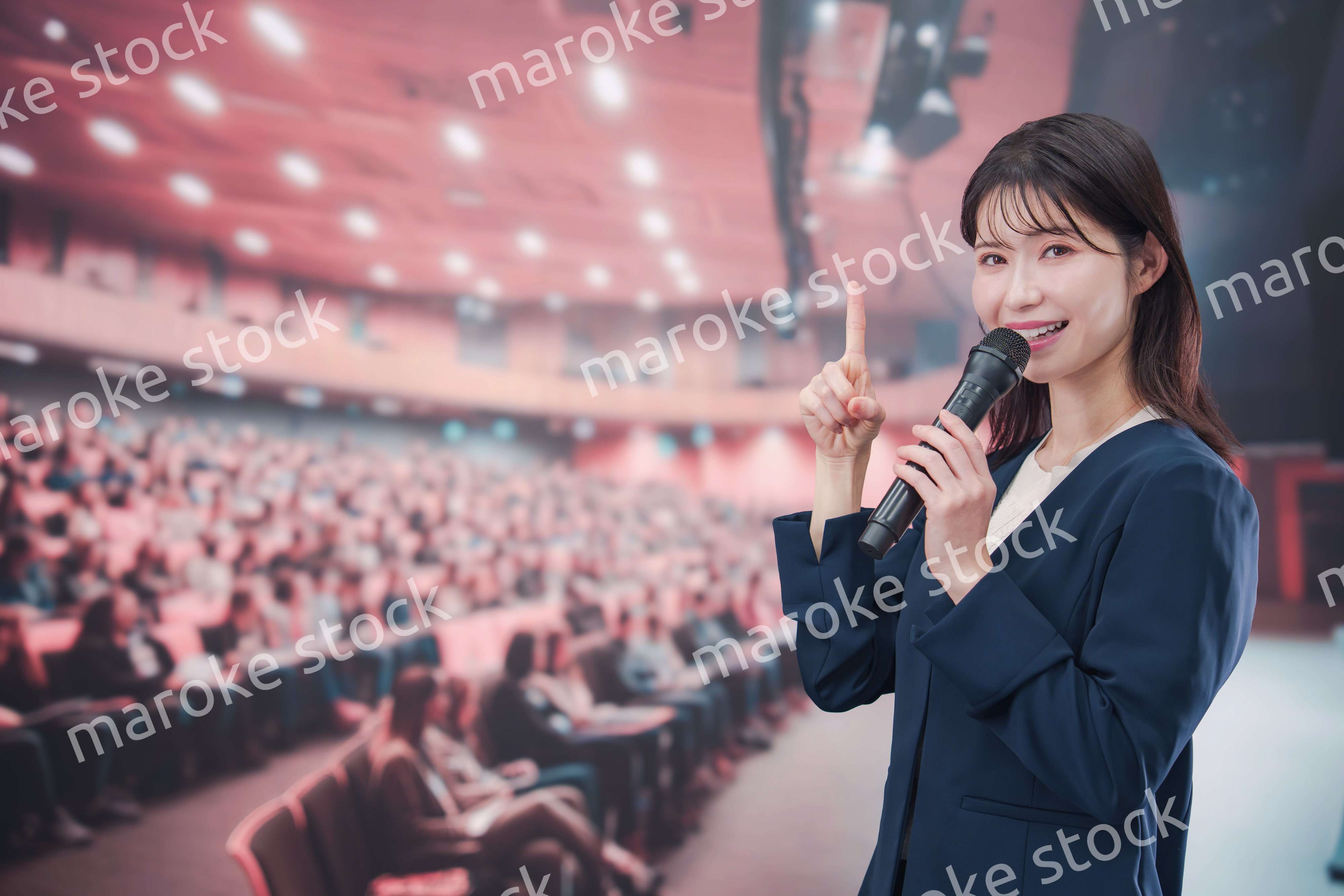 大勢の聴衆が集まるホールで司会をする若い女性