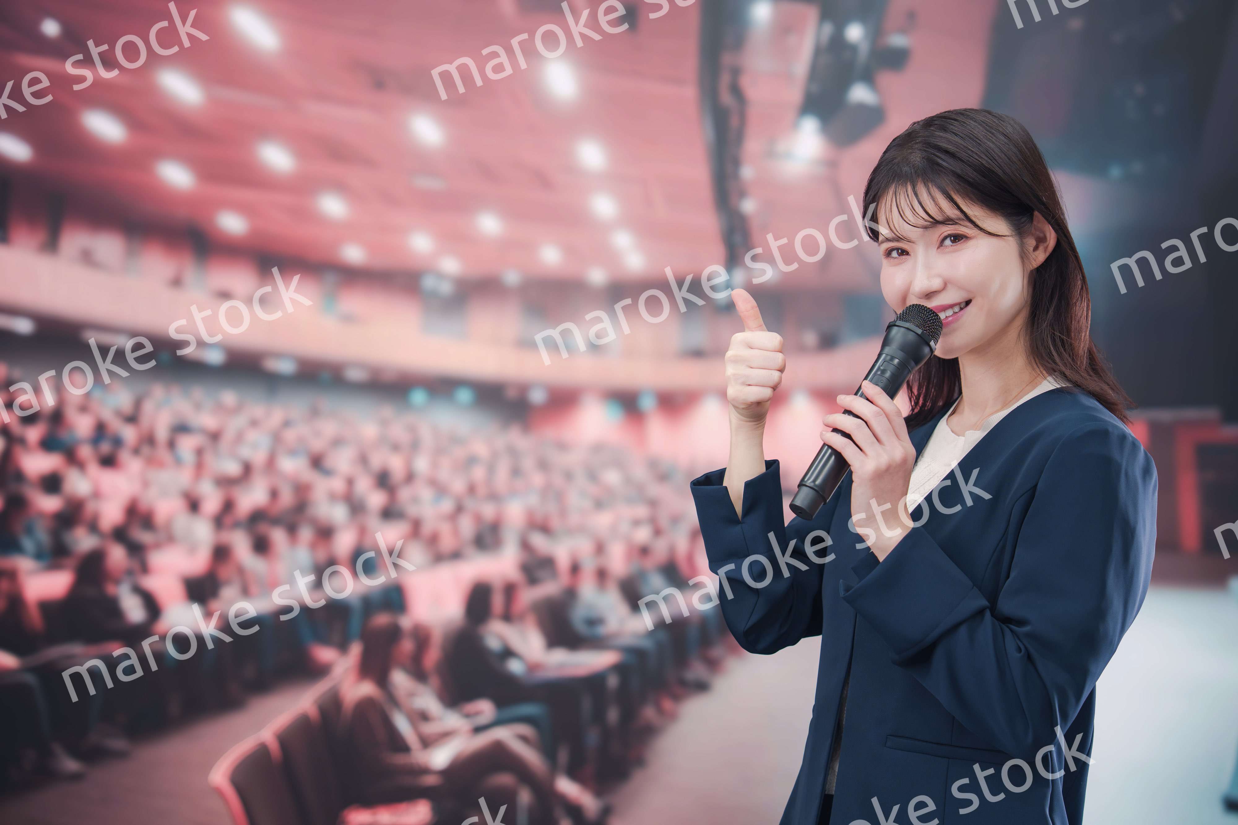 大勢の聴衆が集まるホールで司会をする若い女性