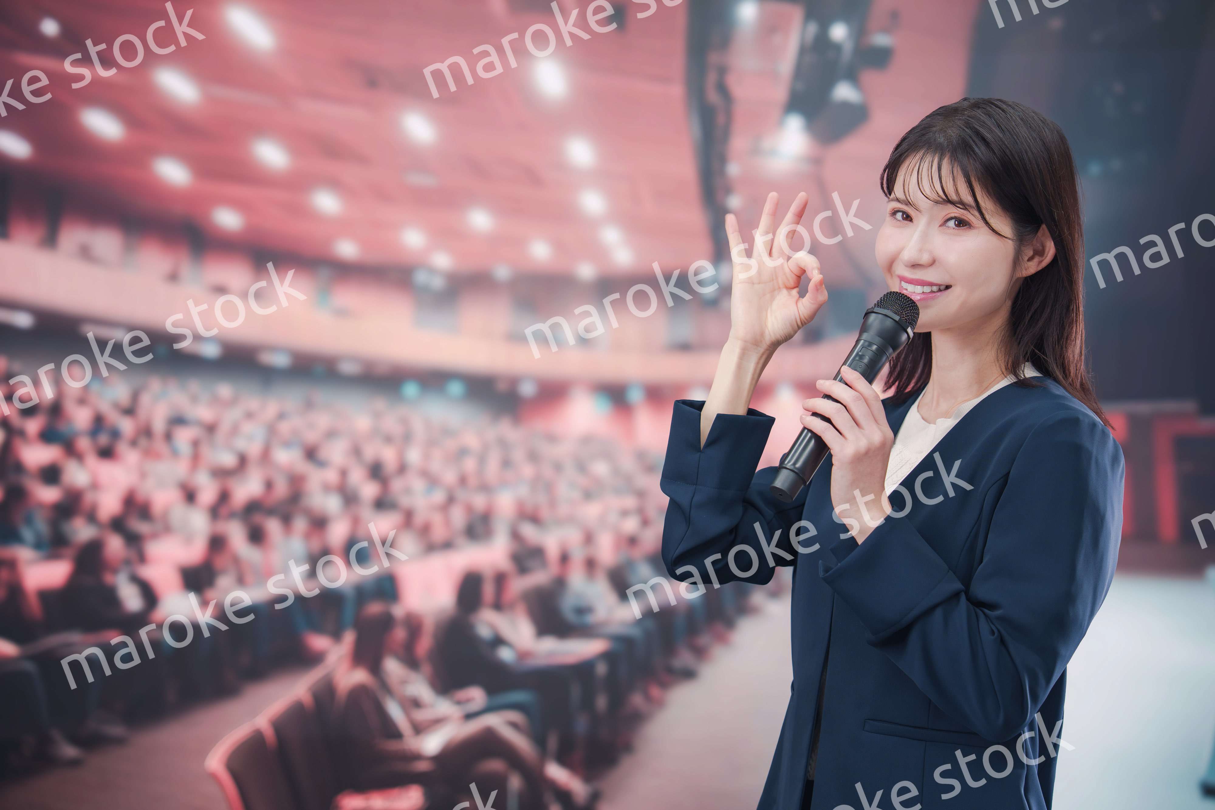 大勢の聴衆が集まるホールで司会をする若い女性