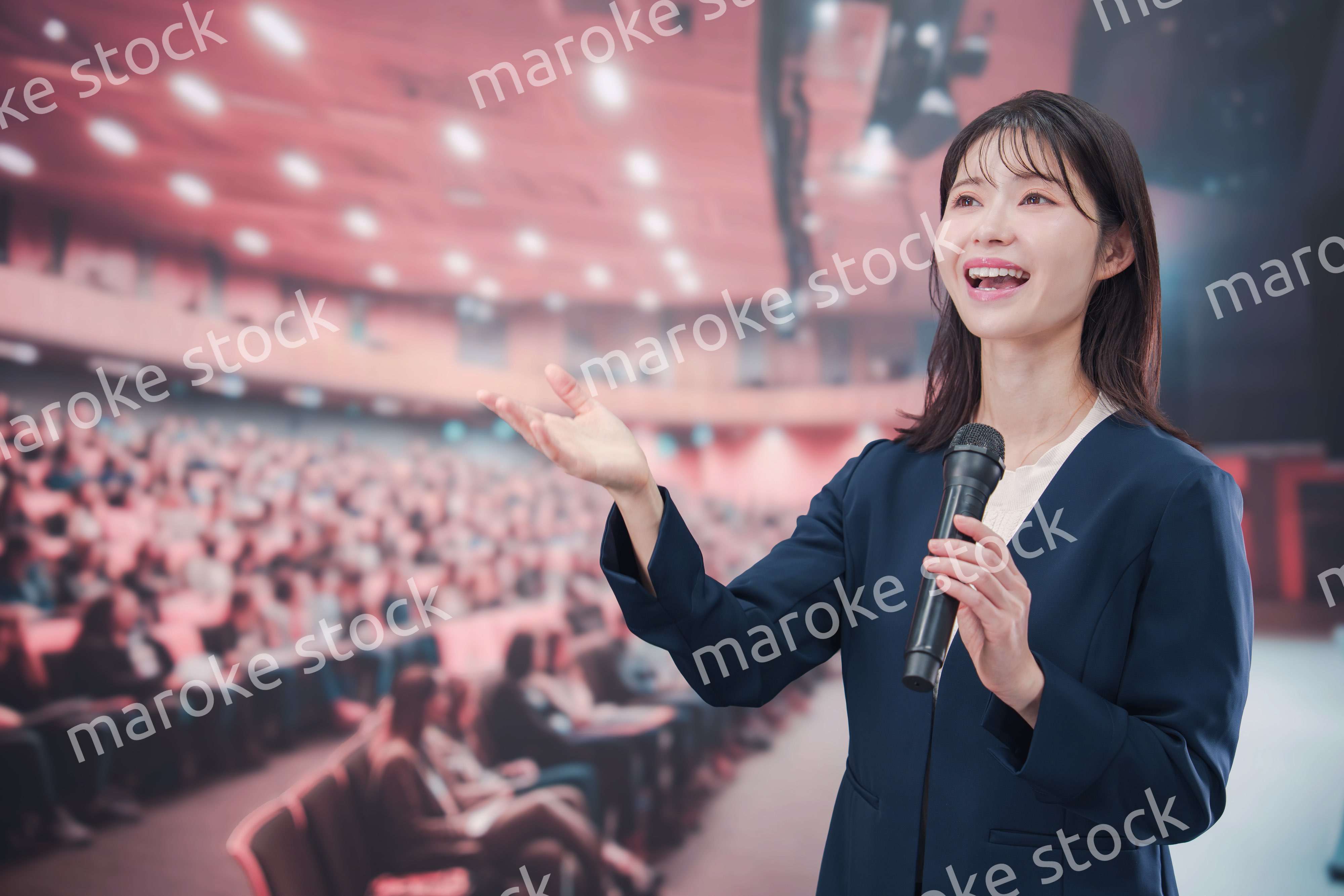 大勢の聴衆が集まるホールで司会をする若い女性