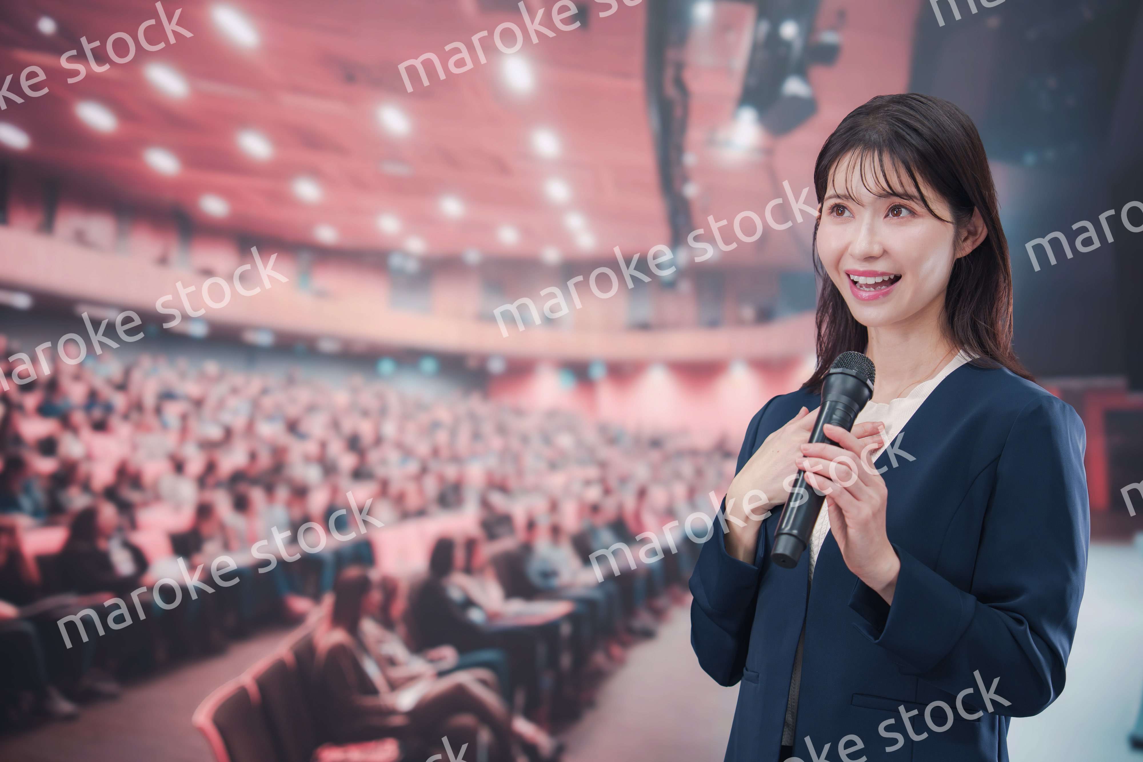 大勢の聴衆が集まるホールで司会をする若い女性