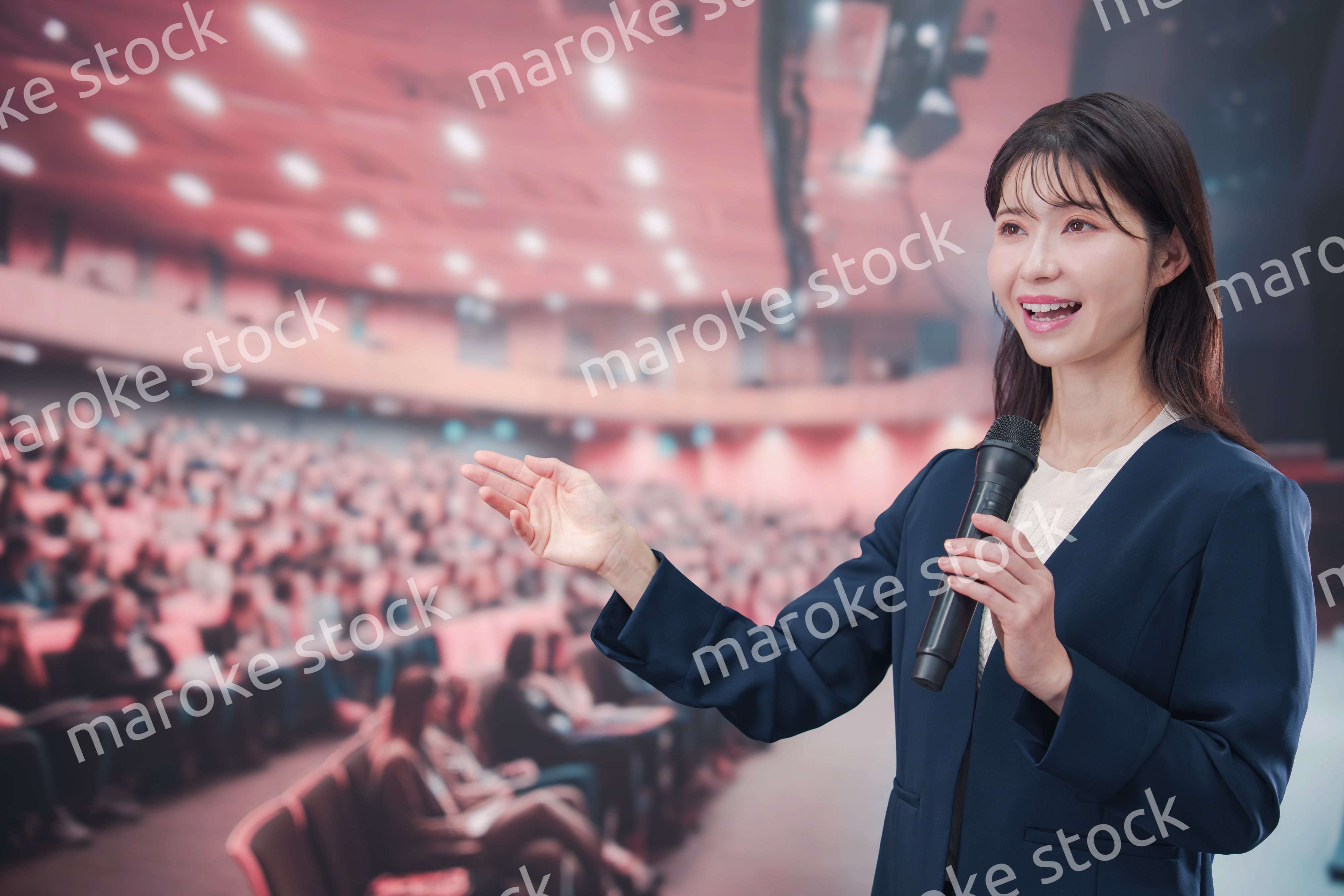 大勢の聴衆が集まるホールで司会をする若い女性