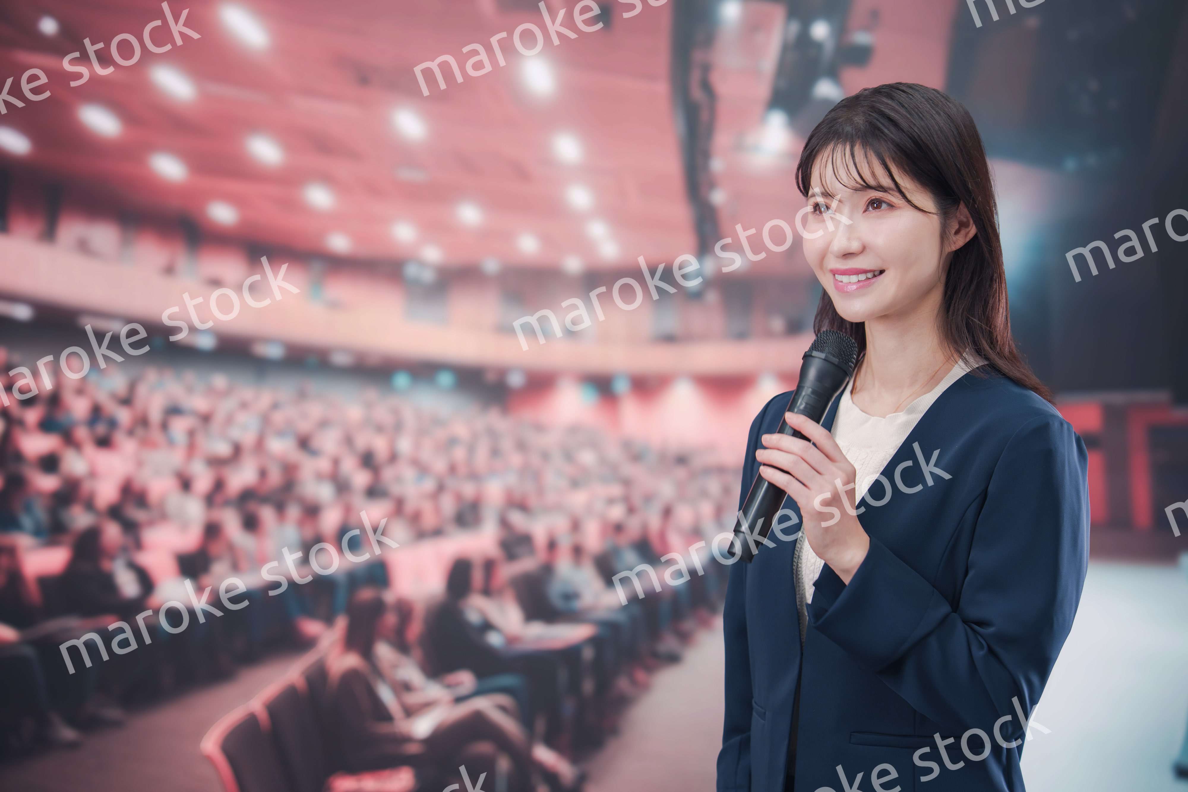 大勢の聴衆が集まるホールで司会をする若い女性