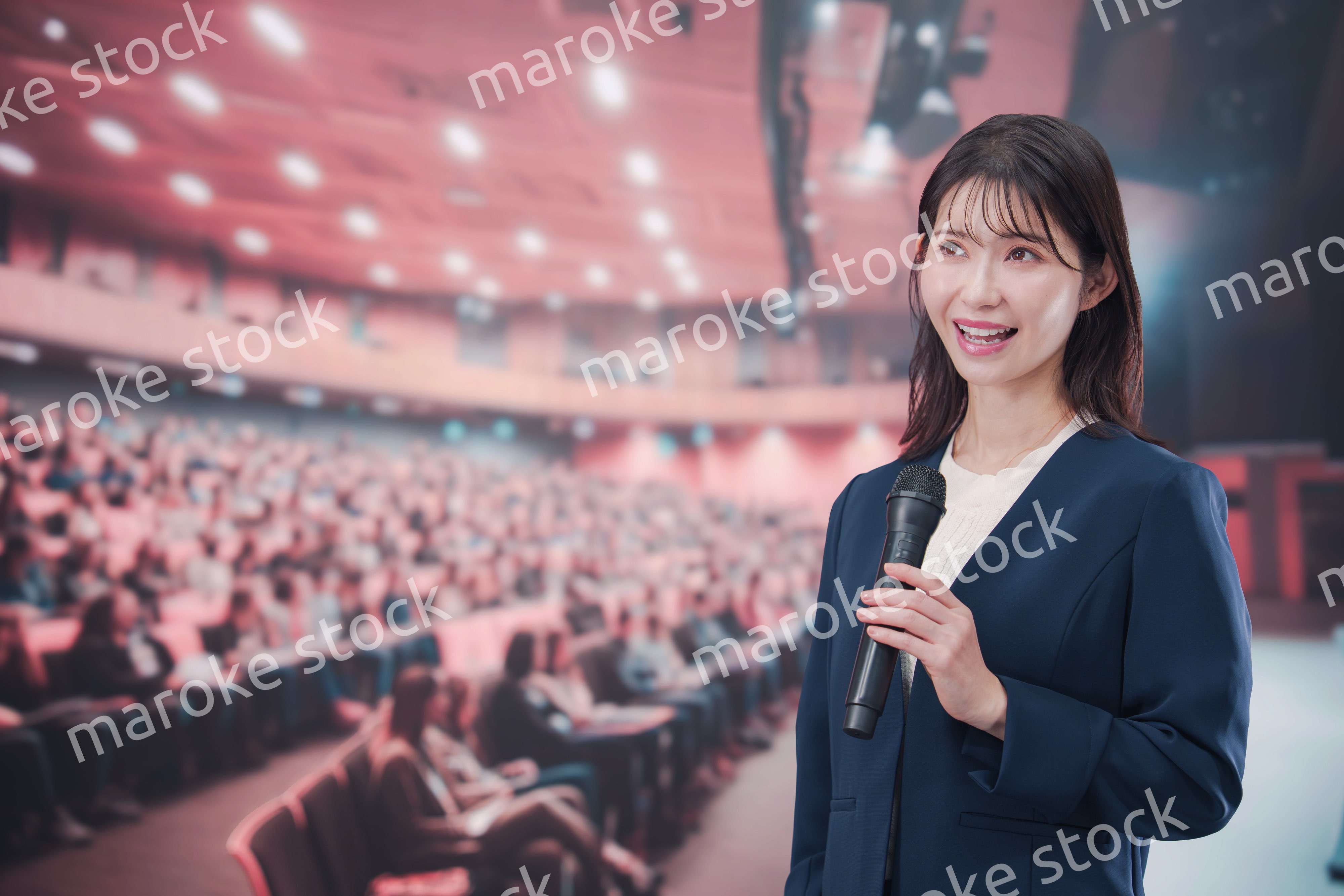 大勢の聴衆が集まるホールで司会をする若い女性