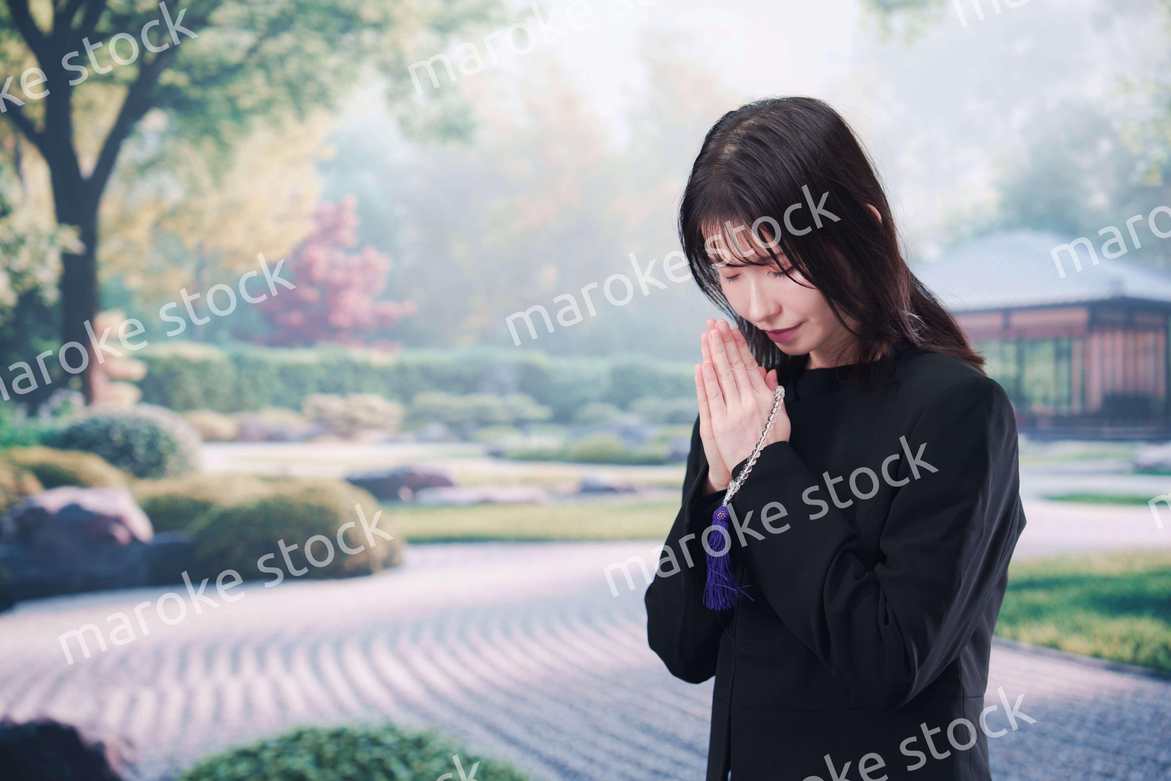 喪服を着て数珠を持って手を合わせる女性