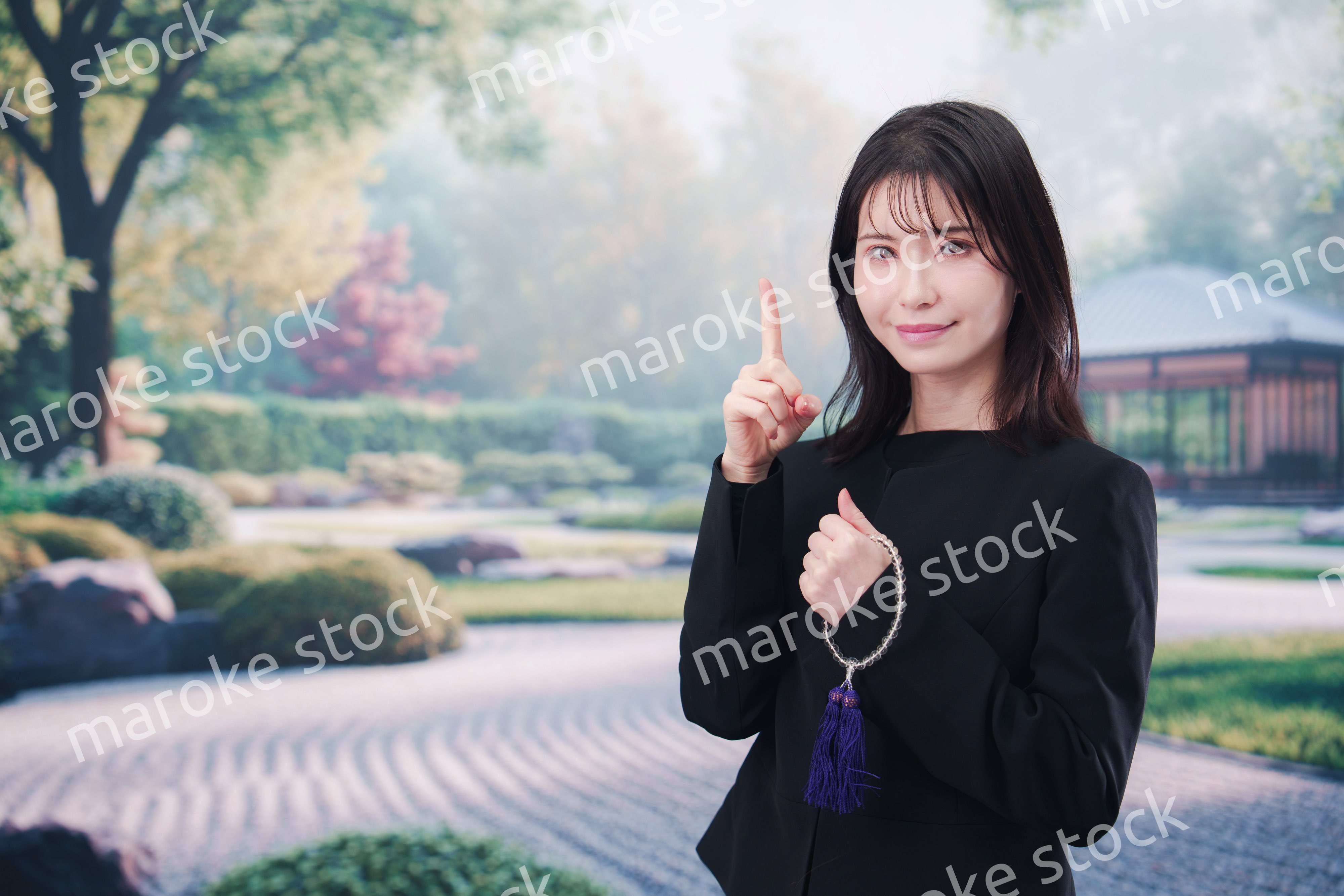 喪服を着て数珠を持って手を合わせる女性