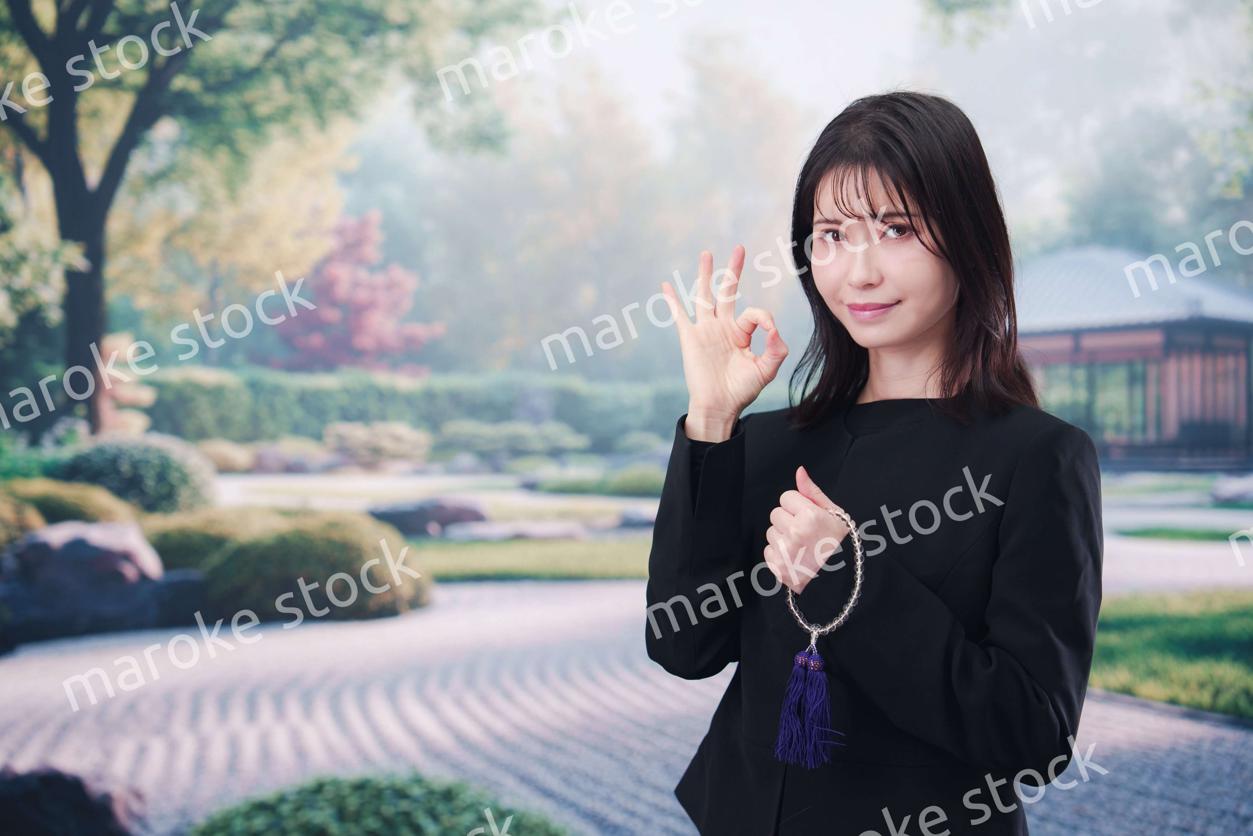 喪服を着て数珠を持って手を合わせる女性